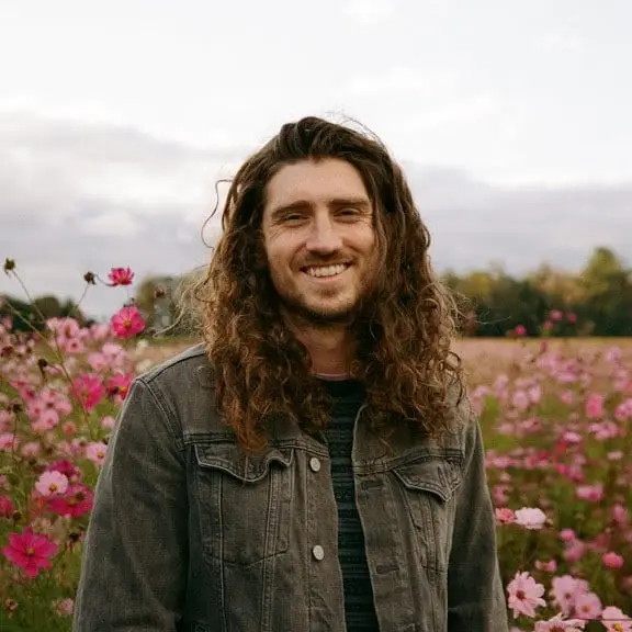 Brennan Dugan, founder of White Lion Wedding Photography, standing in a field of pink flowers