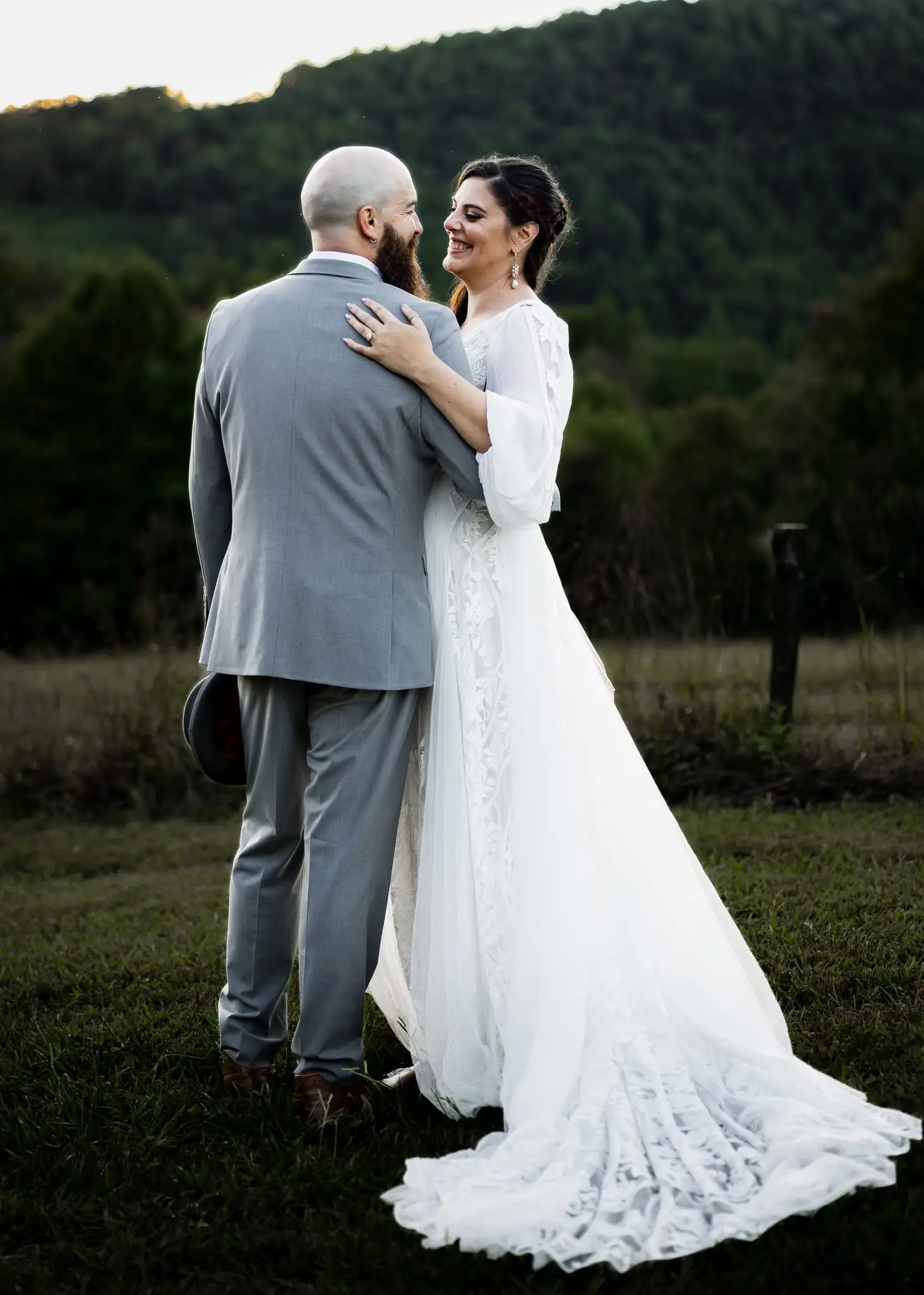 Bride and groom embracing in a mountain meadow near Asheville, seen from behind with forested hills beyond