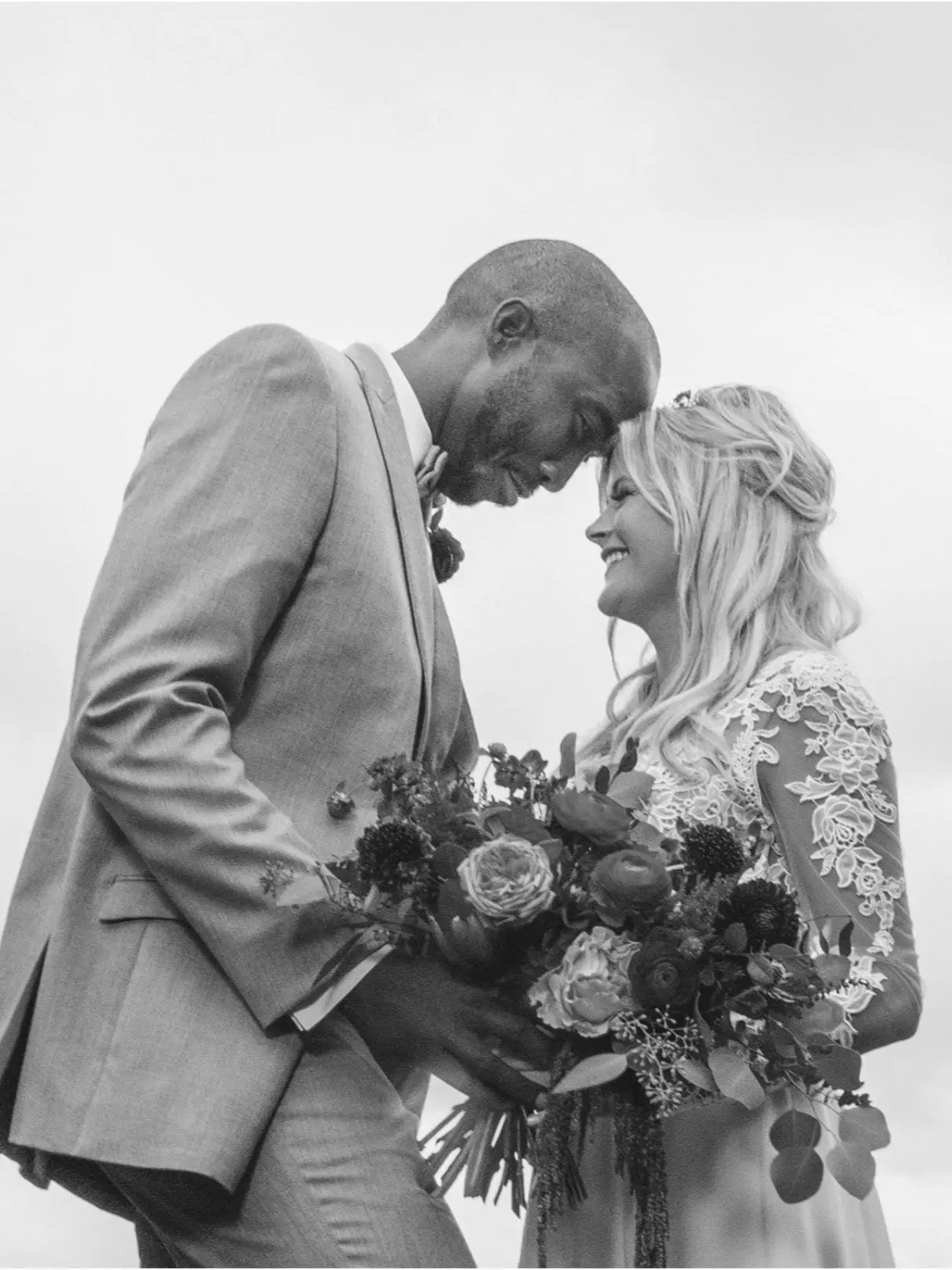 Charlie and Olivia forehead to forehead holding a bouquet, in black and white