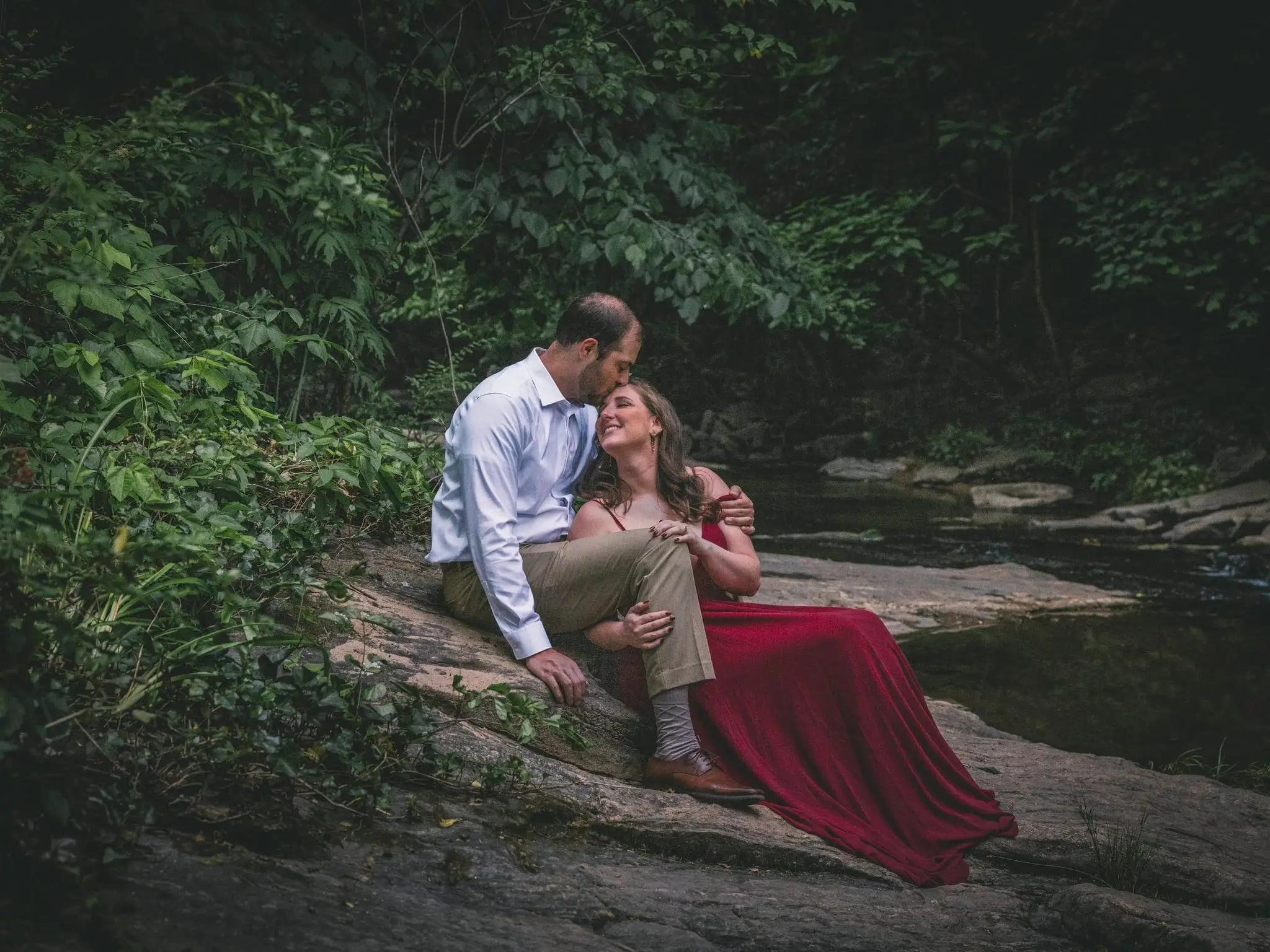 An engaged couple sitting on mossy rocks in a forest near Asheville