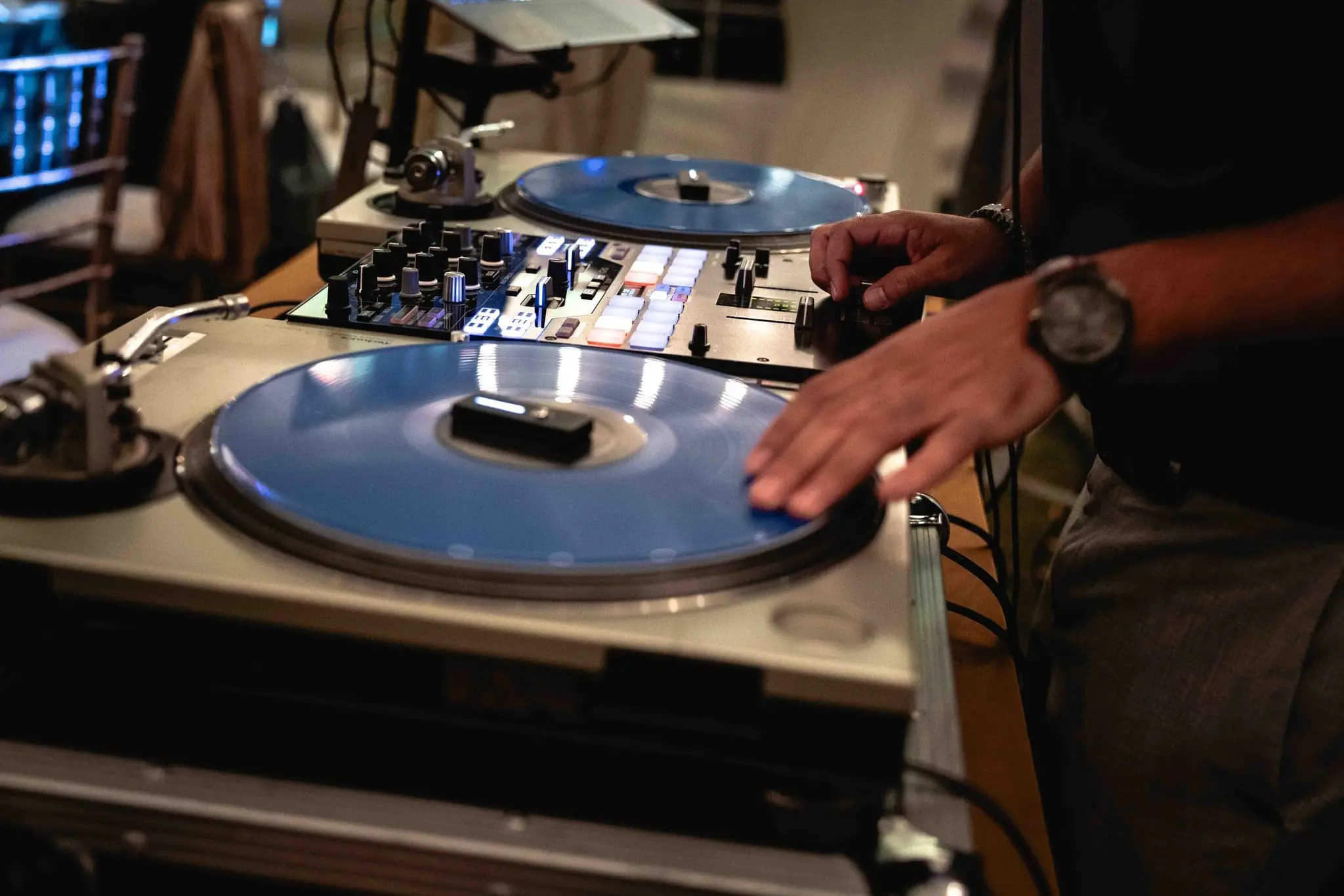 DJ's hand on a turntable with blue vinyl beside a mixer
