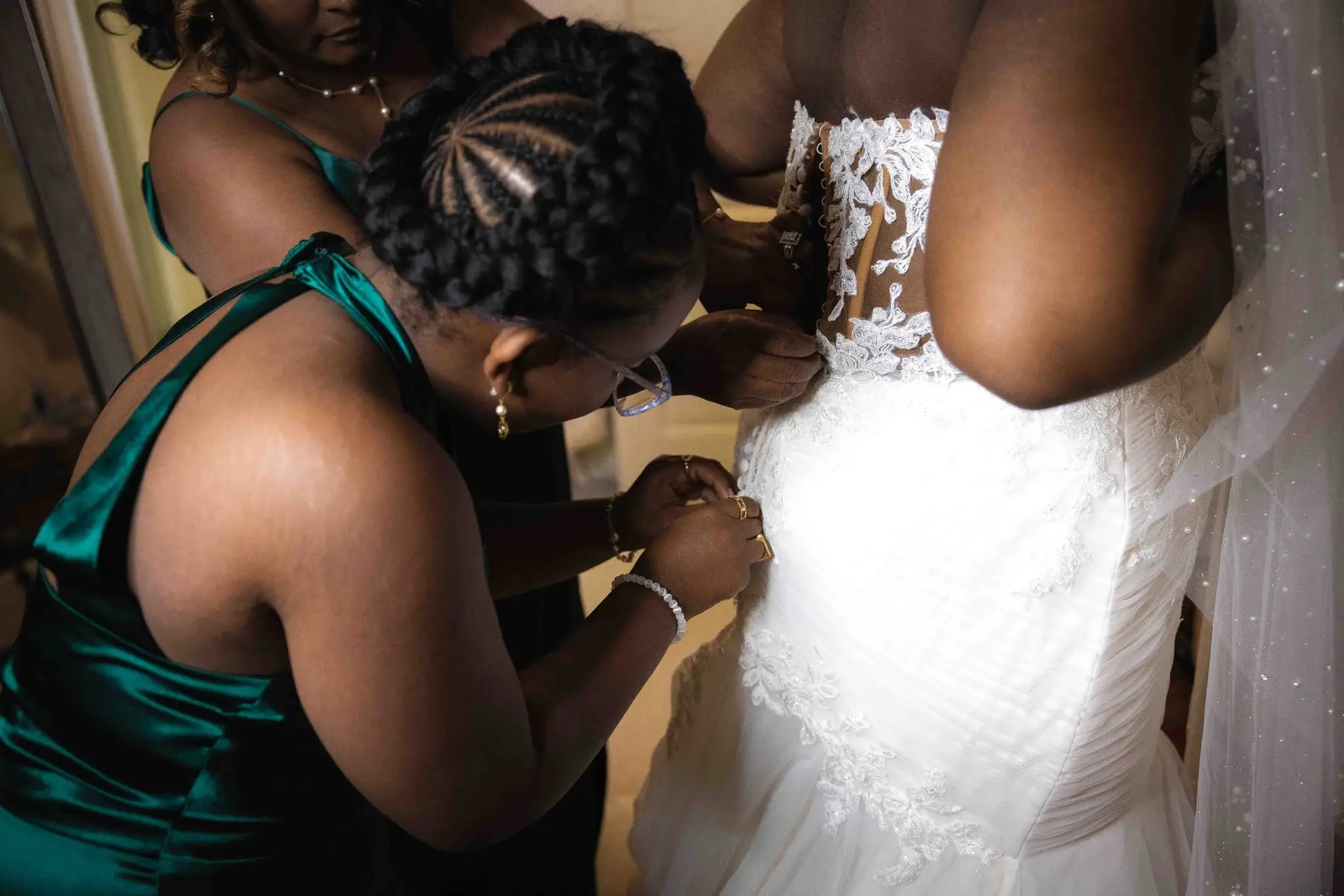 Bridesmaids in emerald satin helping fasten the back of the bride's lace gown