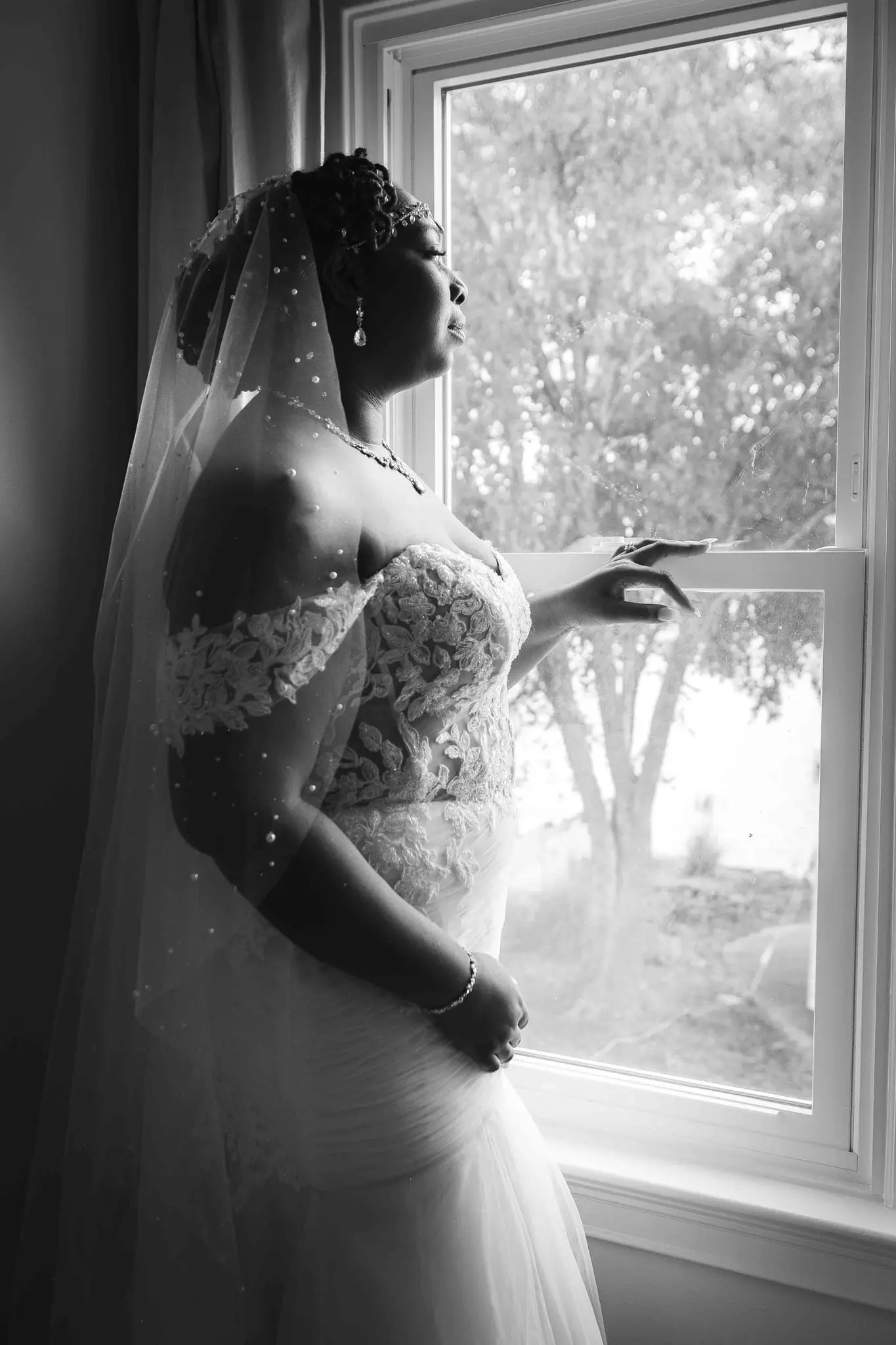 Black and white profile of the bride at a window, veil and lace sleeves framing her face
