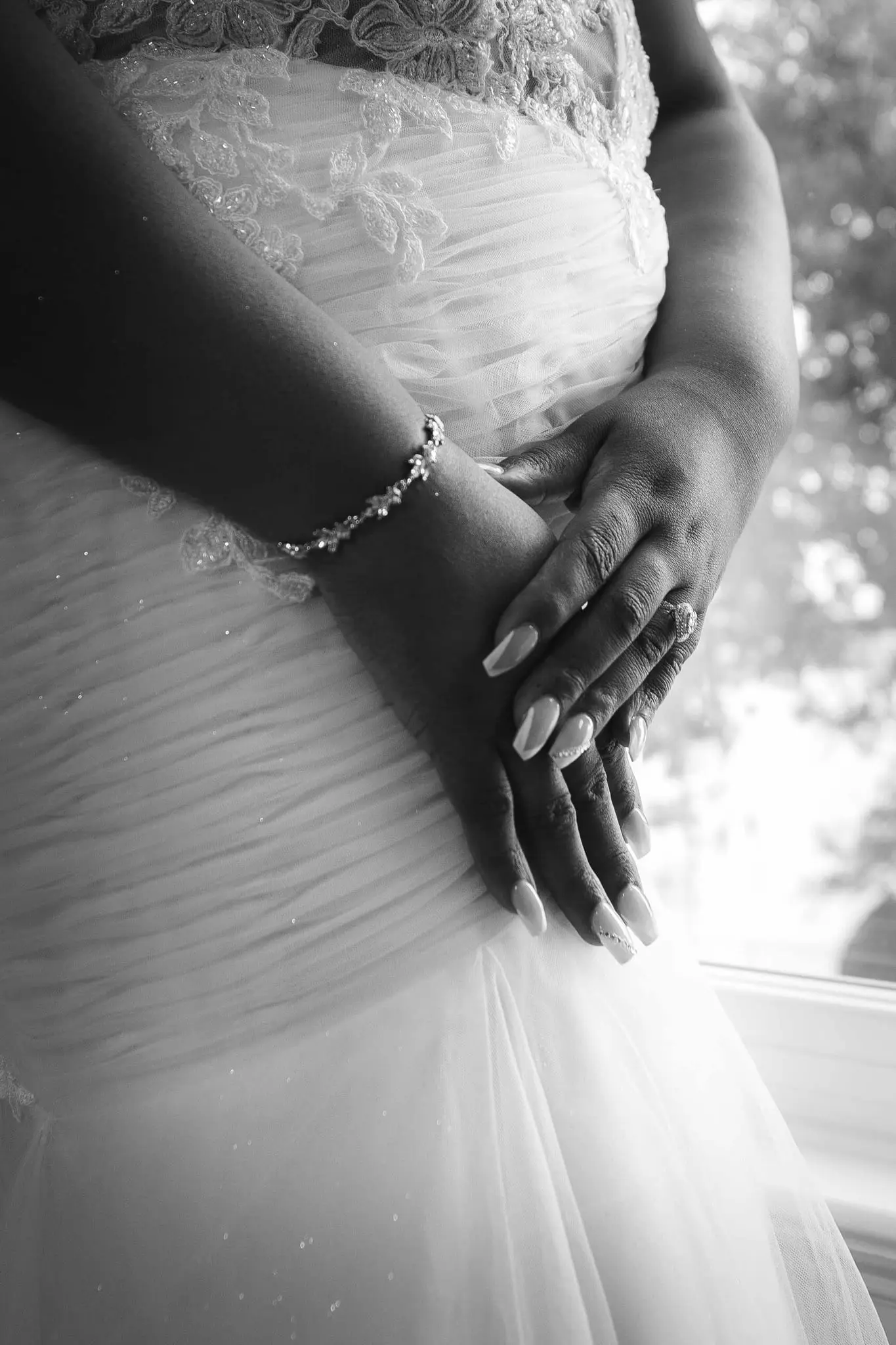 Black and white detail of the bride's folded hands, bracelet and ring against her ruched gown