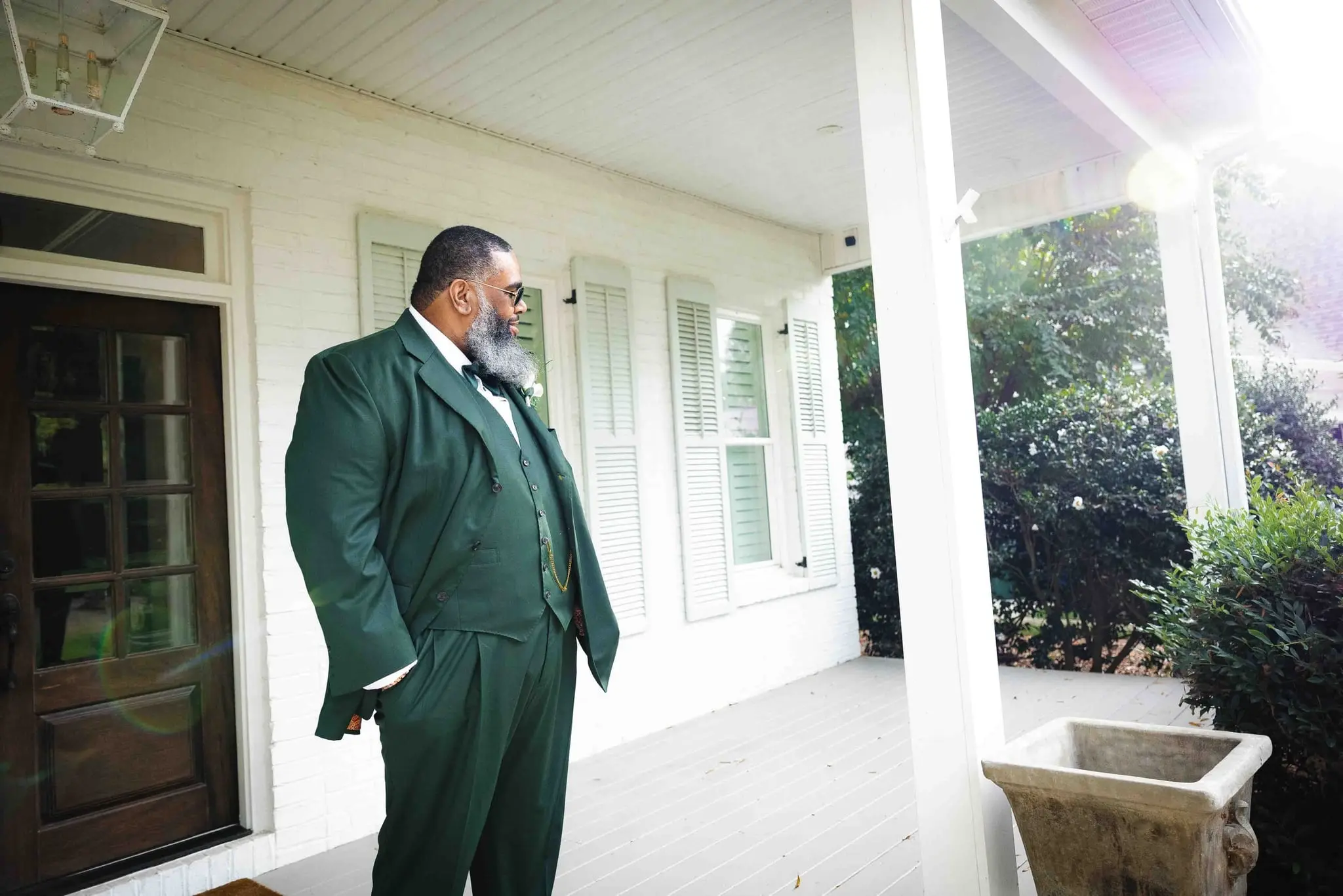 Groom in a green suit waiting alone on a white porch, hands in his pockets