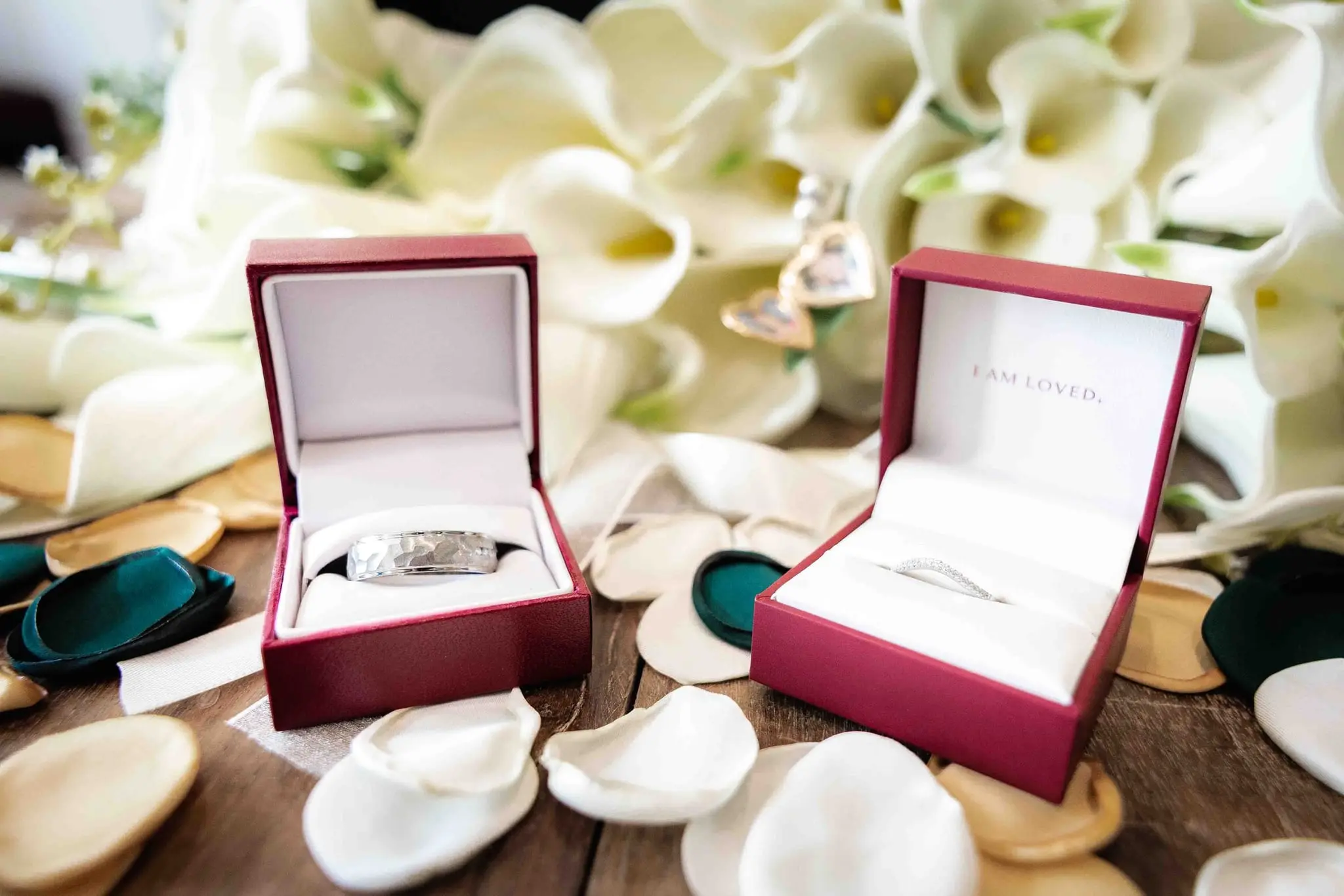 Two wedding rings in red ring boxes among white calla lilies and gold and green petals