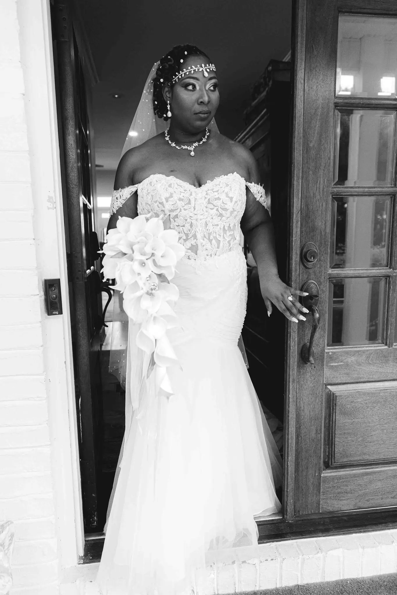 Black and white portrait of the bride in a doorway holding her cascading calla lily bouquet