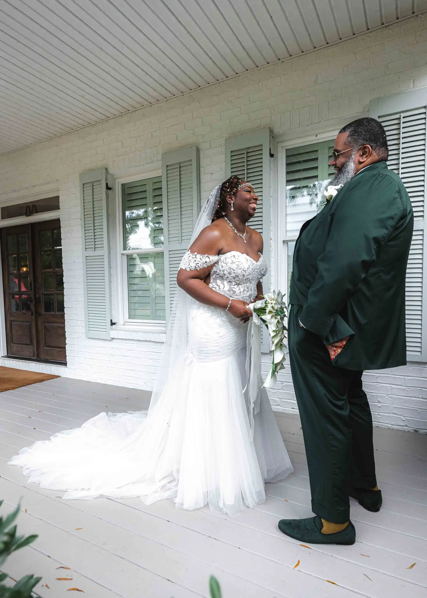 Couple sharing a smile across the porch during their first look, her long train spread behind