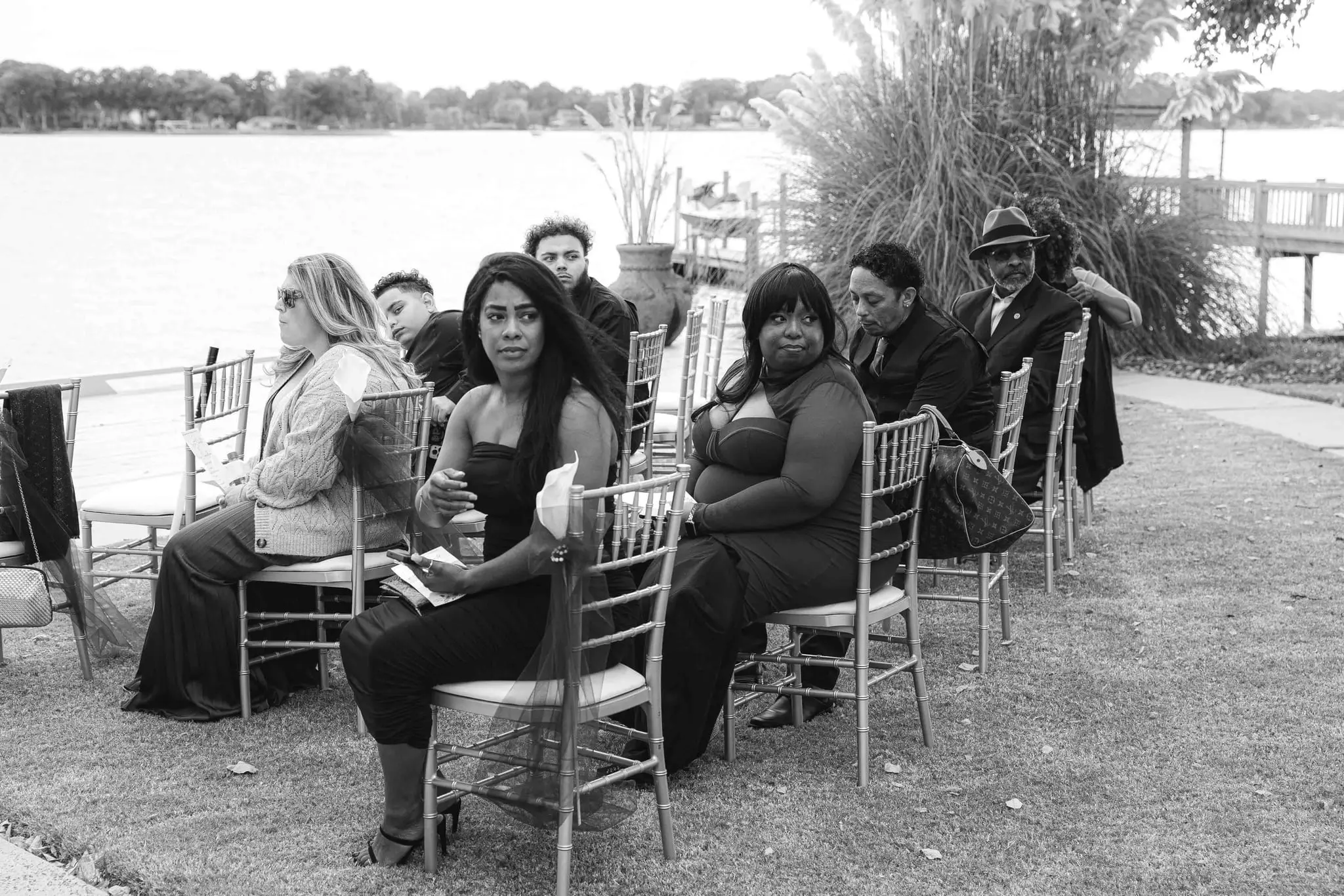 Black and white shot of guests seated on gold chairs by the lake before the ceremony