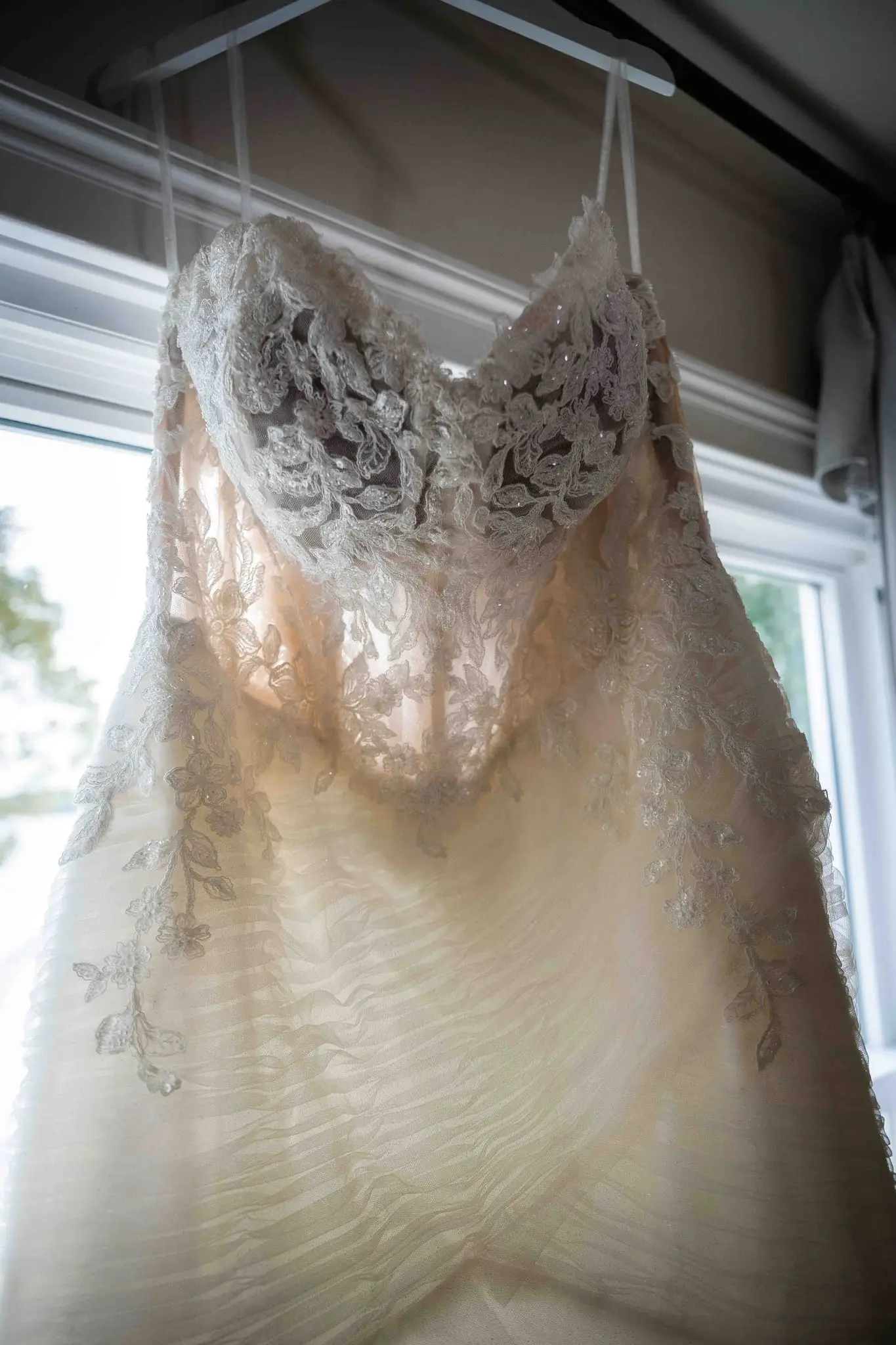Lace wedding gown hanging in a sunlit window