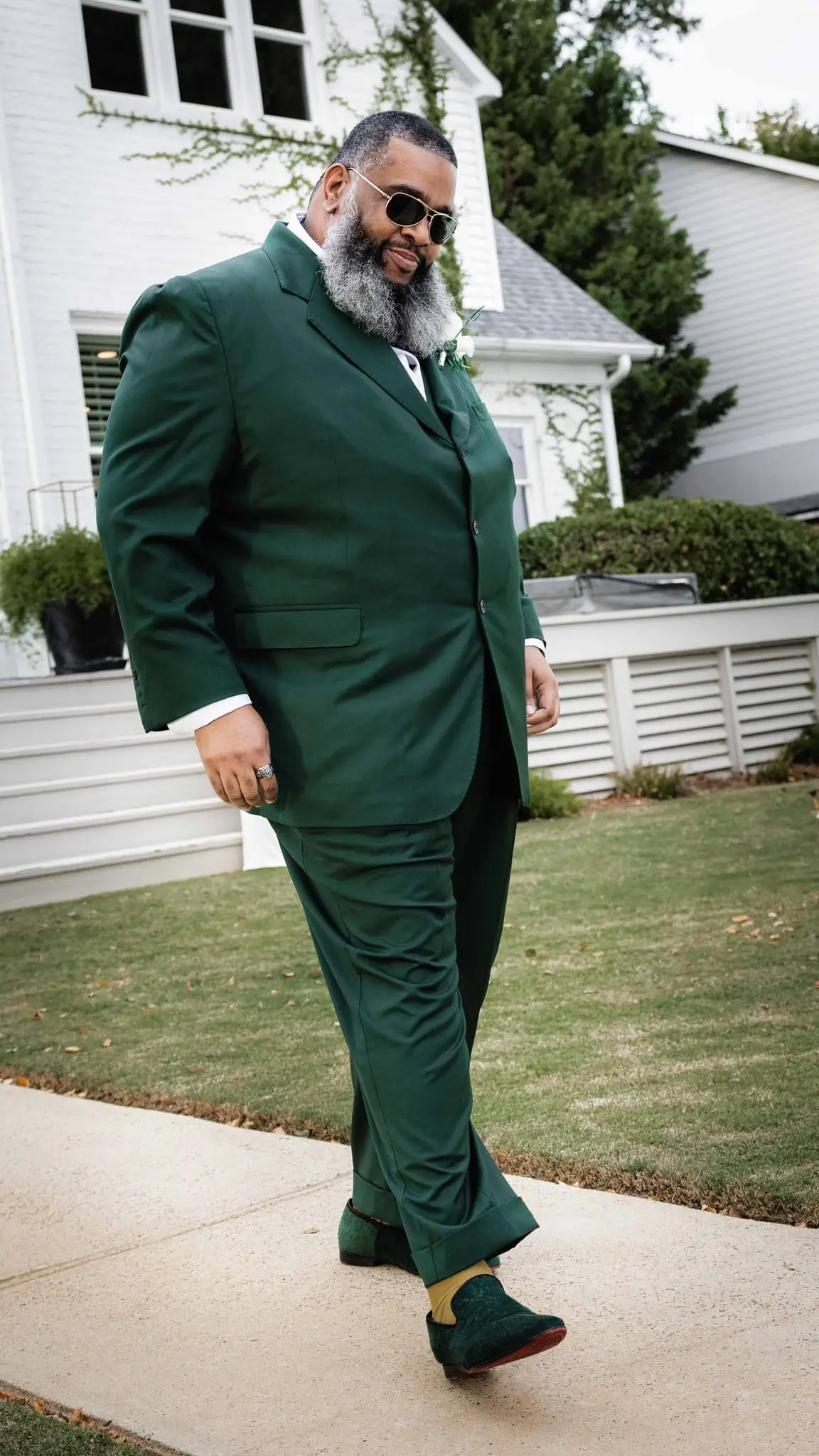 Groom in sunglasses and green velvet loafers walking along the garden path