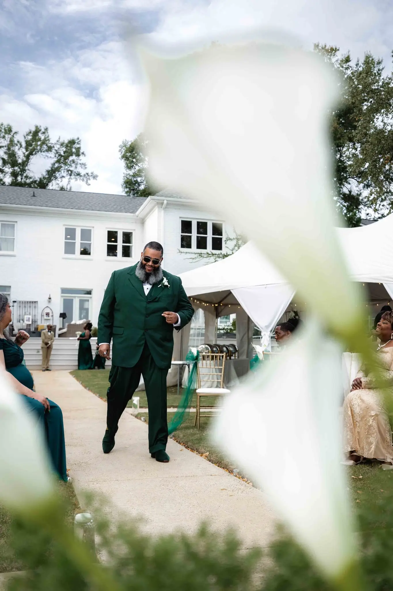 Groom in green walking toward the ceremony past a blurred calla lily in the foreground