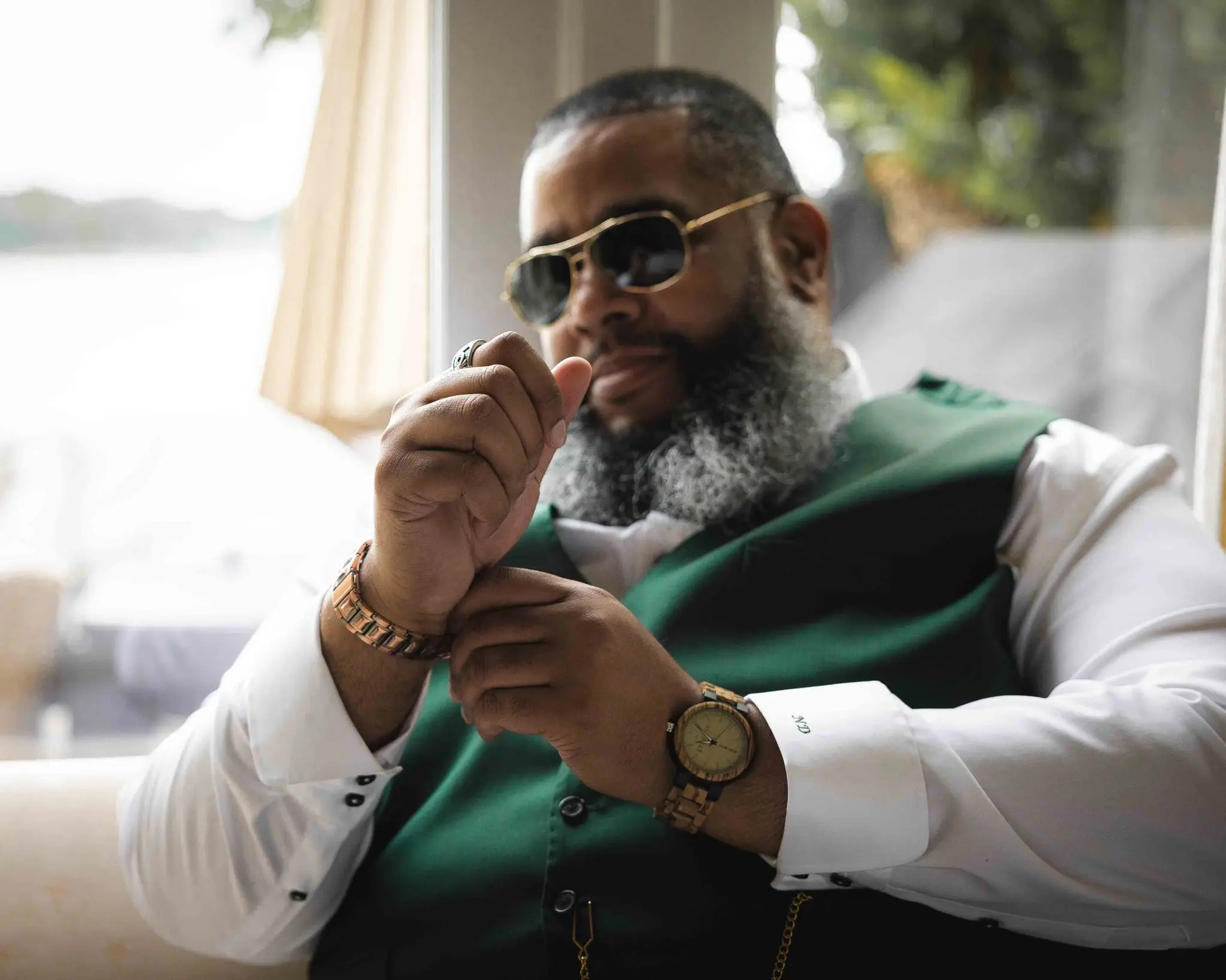Groom in sunglasses and a green vest adjusting his watch cuff