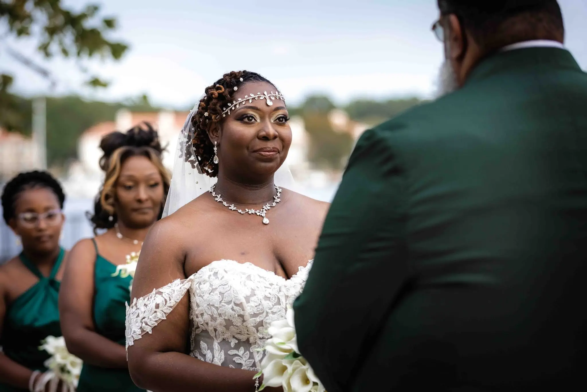 Bride looking ahead with a calm smile as bridesmaids stand behind her at the lakeside ceremony