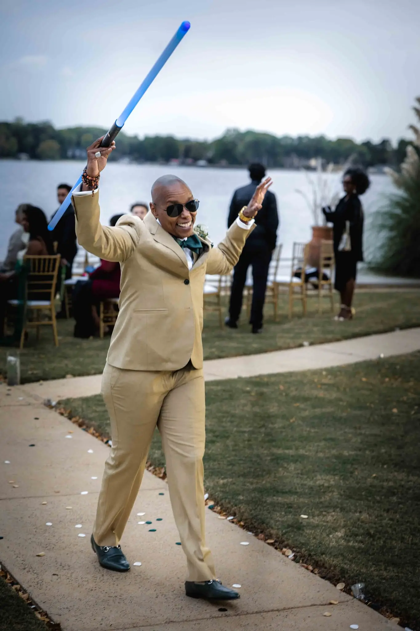 Attendant in a tan suit raising a glowing blue sword in celebration on the lawn path
