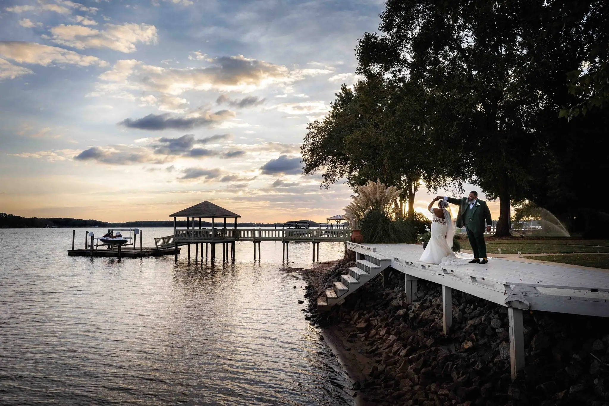 Wide view of the couple dancing on a white pier at Whispering Oaks, a gazebo and golden sky behind