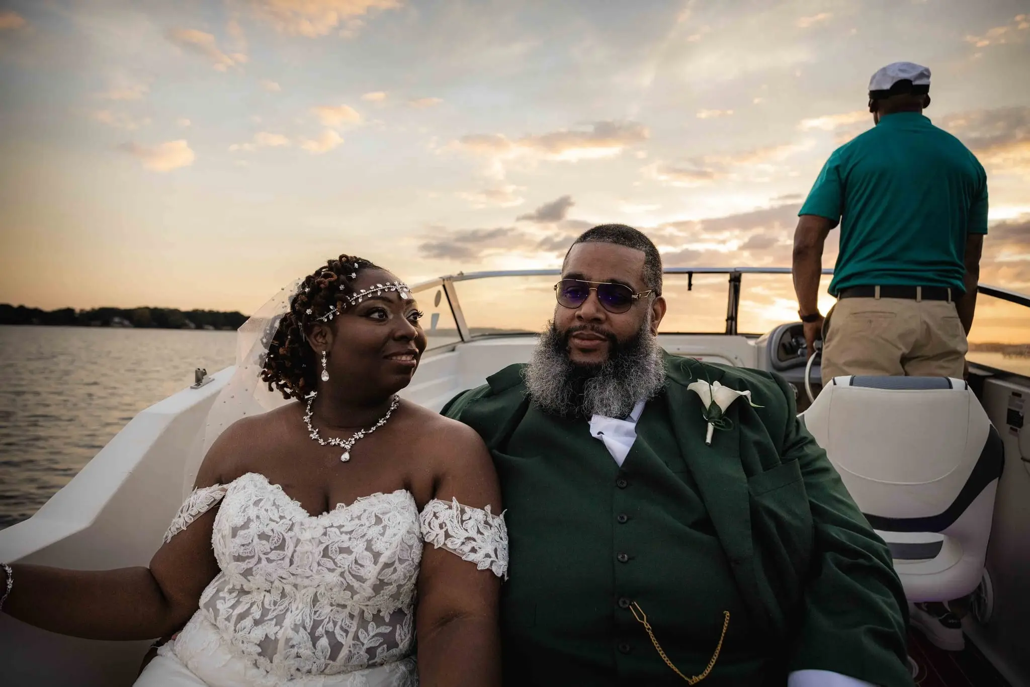 Bride and groom seated on a boat with the captain behind them as sunset glows over the water