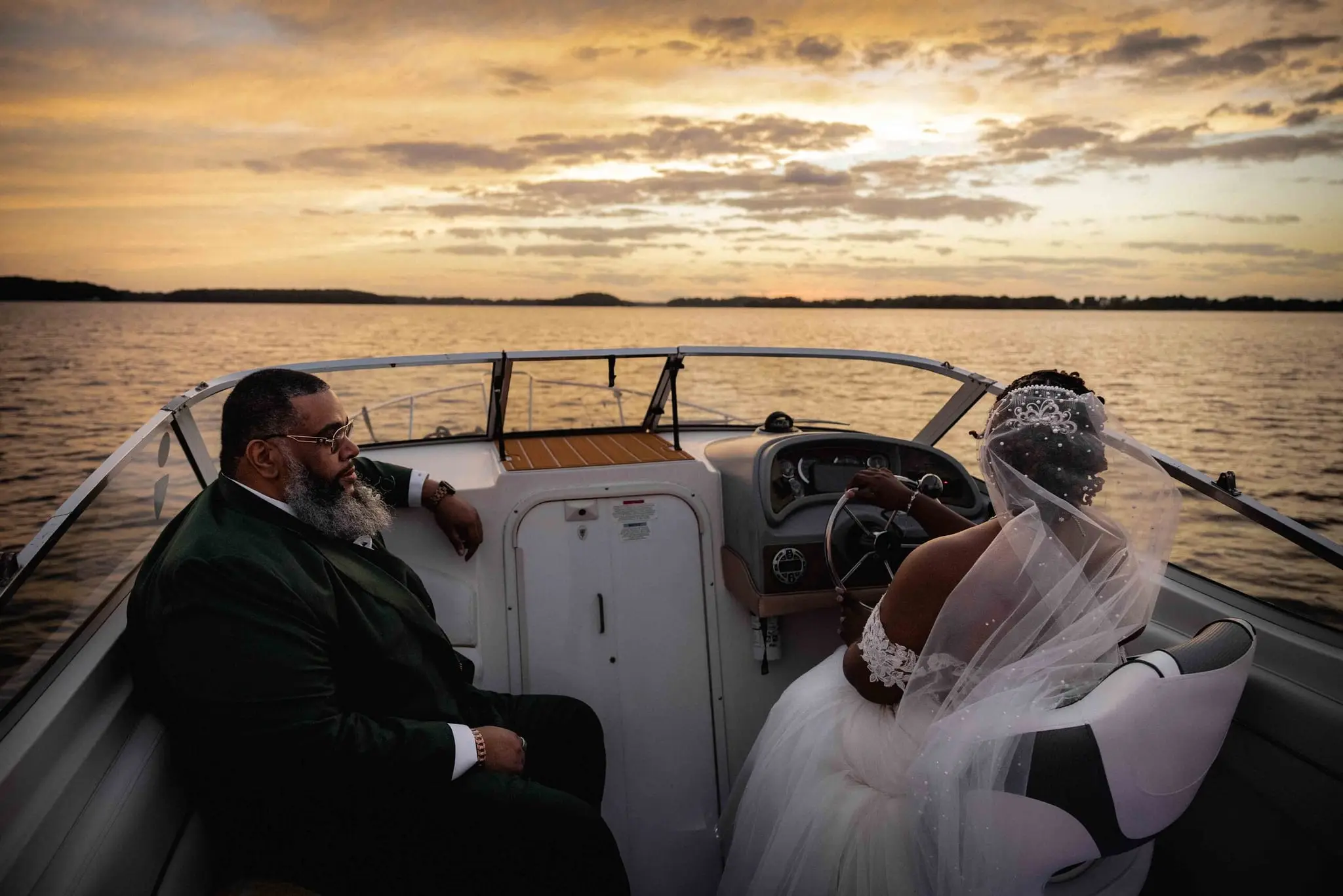 Groom relaxing in a boat seat while the bride drives toward the sunset