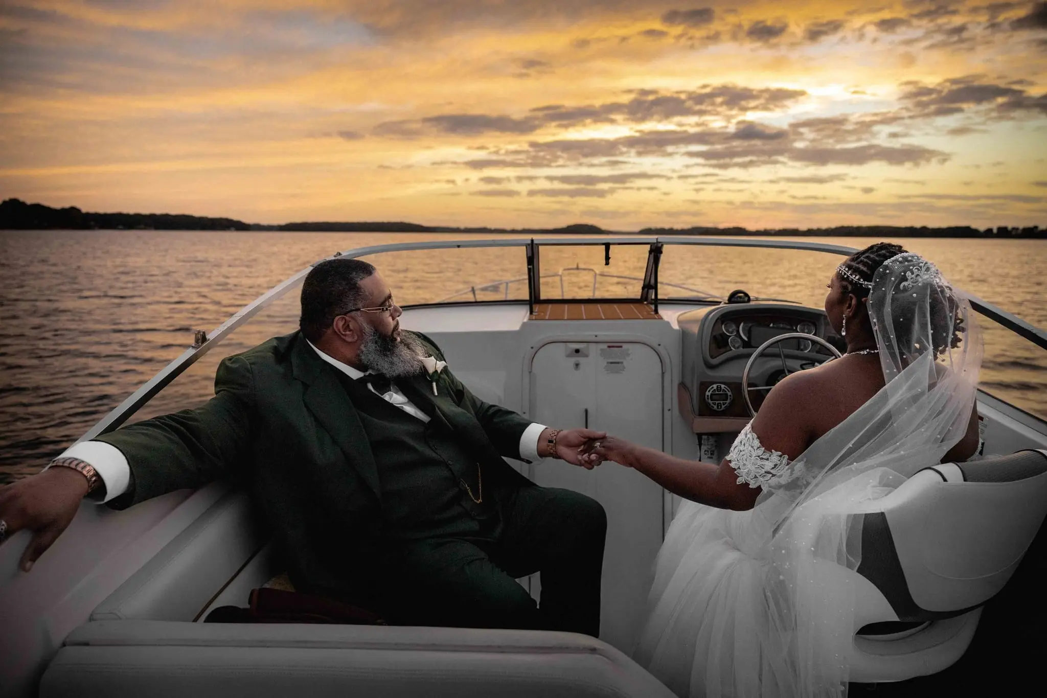Bride at the helm reaching back to hold the groom's hand as the boat cruises into the sunset