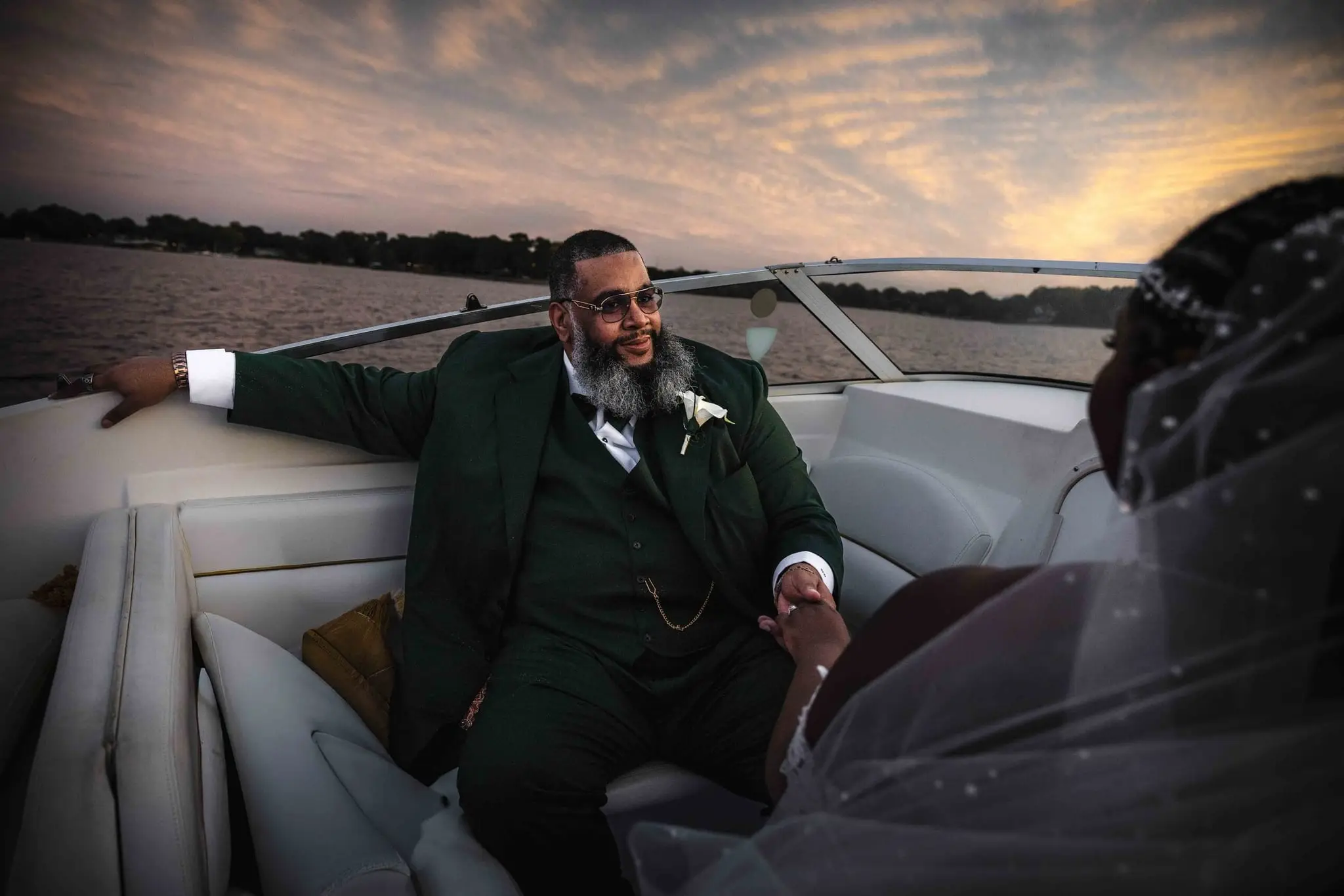 Groom in a green suit stretching an arm along the boat's edge as the bride sits beside him