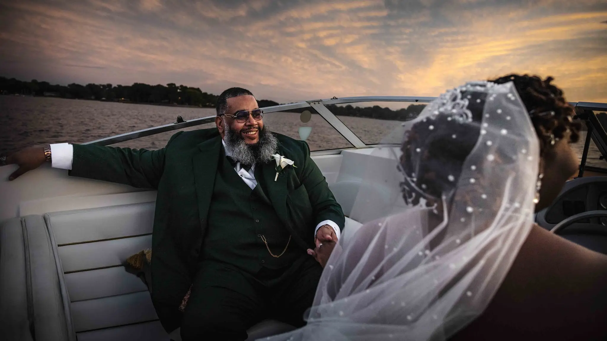 Groom smiling at the bride, her beaded veil in the foreground, on the boat at dusk
