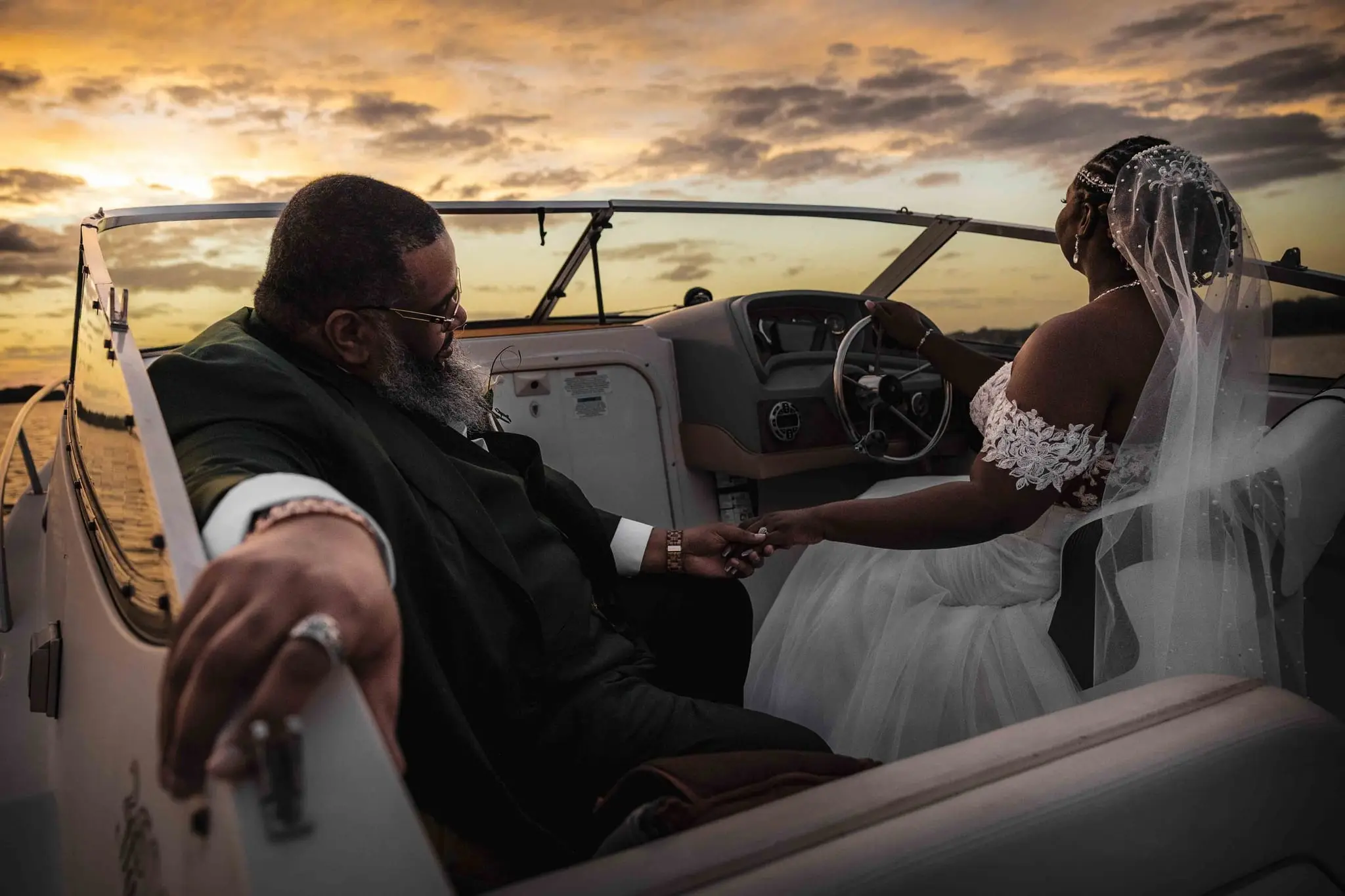 Groom's ringed hand on the boat rail as he holds the bride's hand and she steers