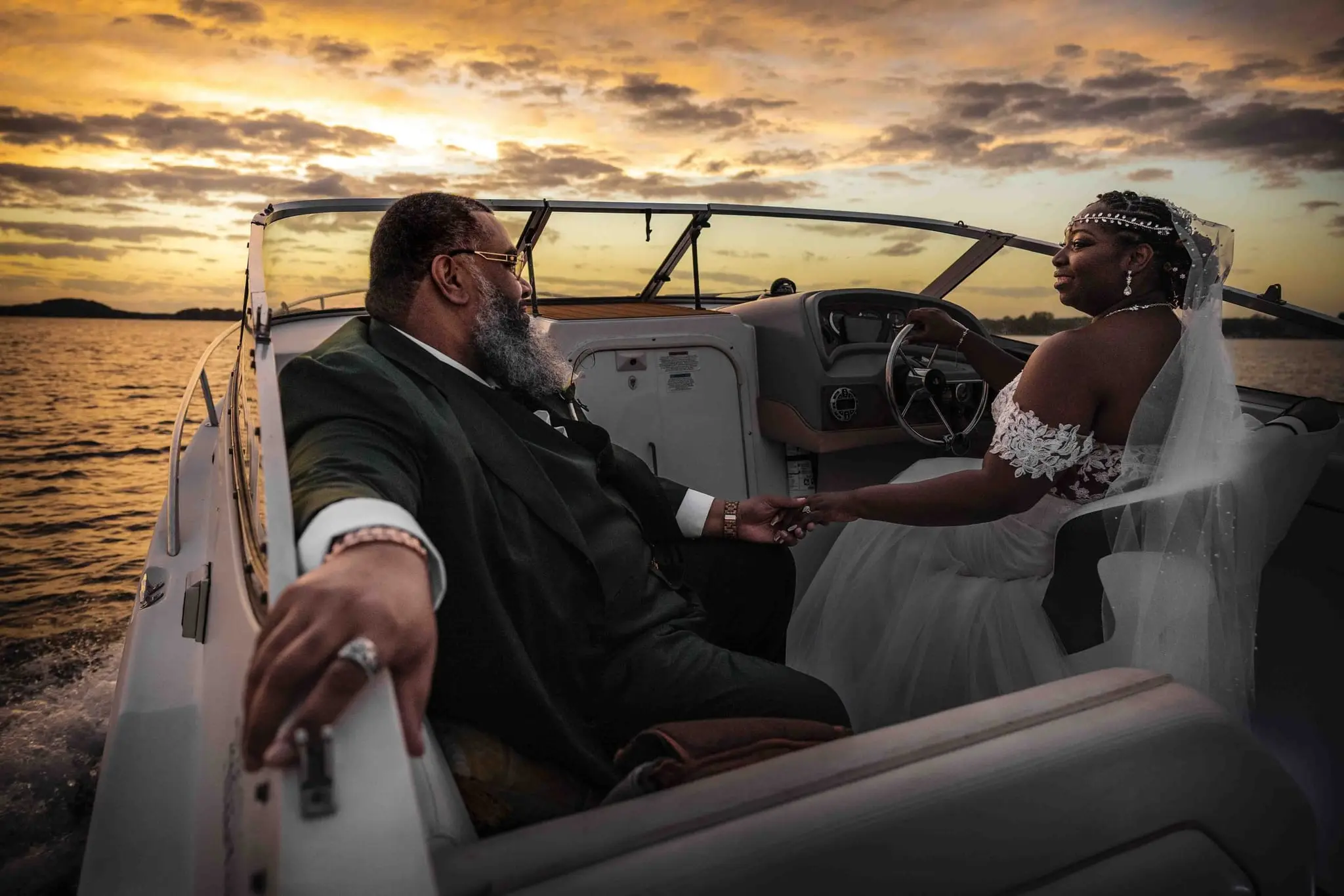 Couple holding hands on a boat while the bride steers and the wake churns behind them