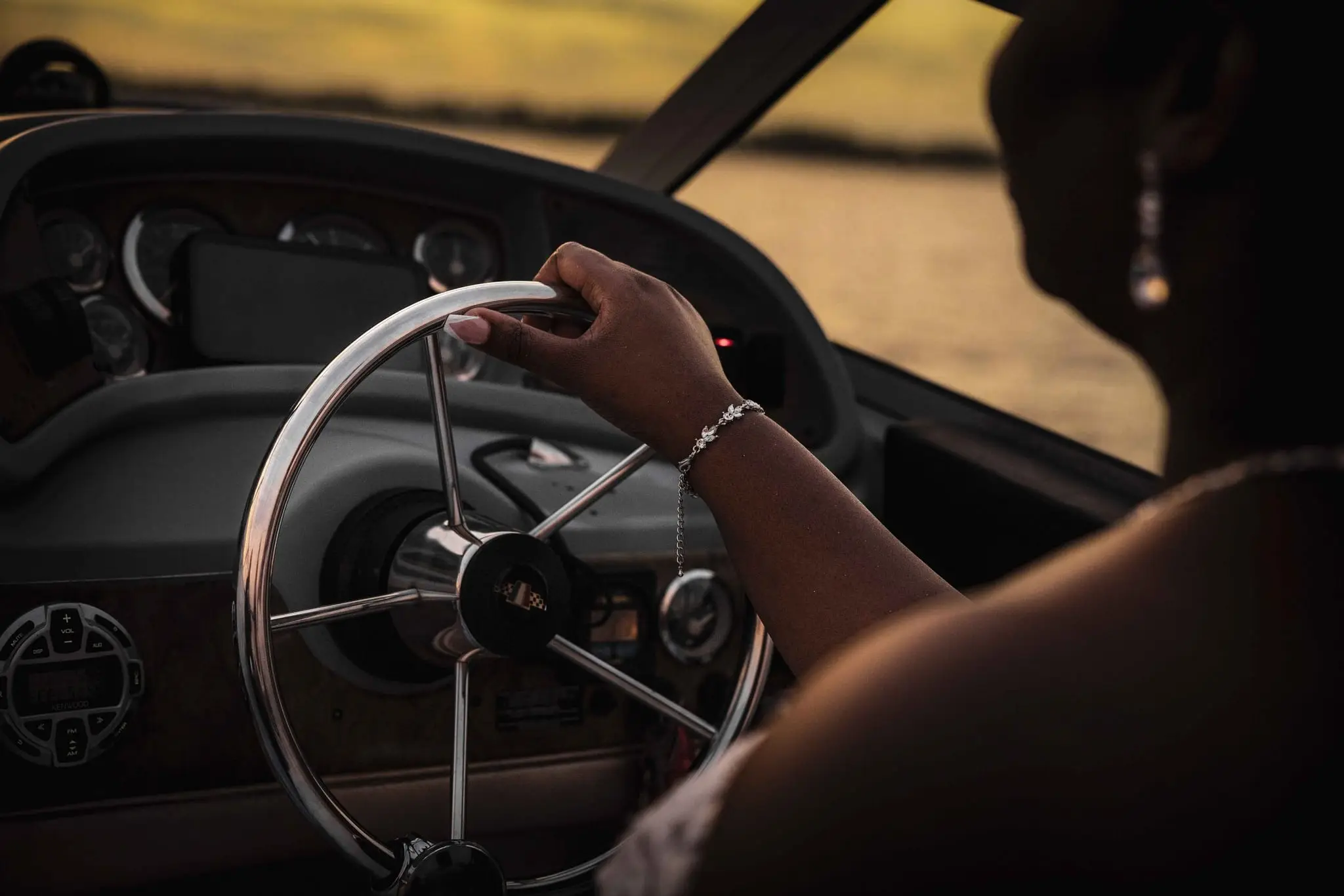 Bride's hand with a pearl bracelet gripping the boat's steering wheel at sunset