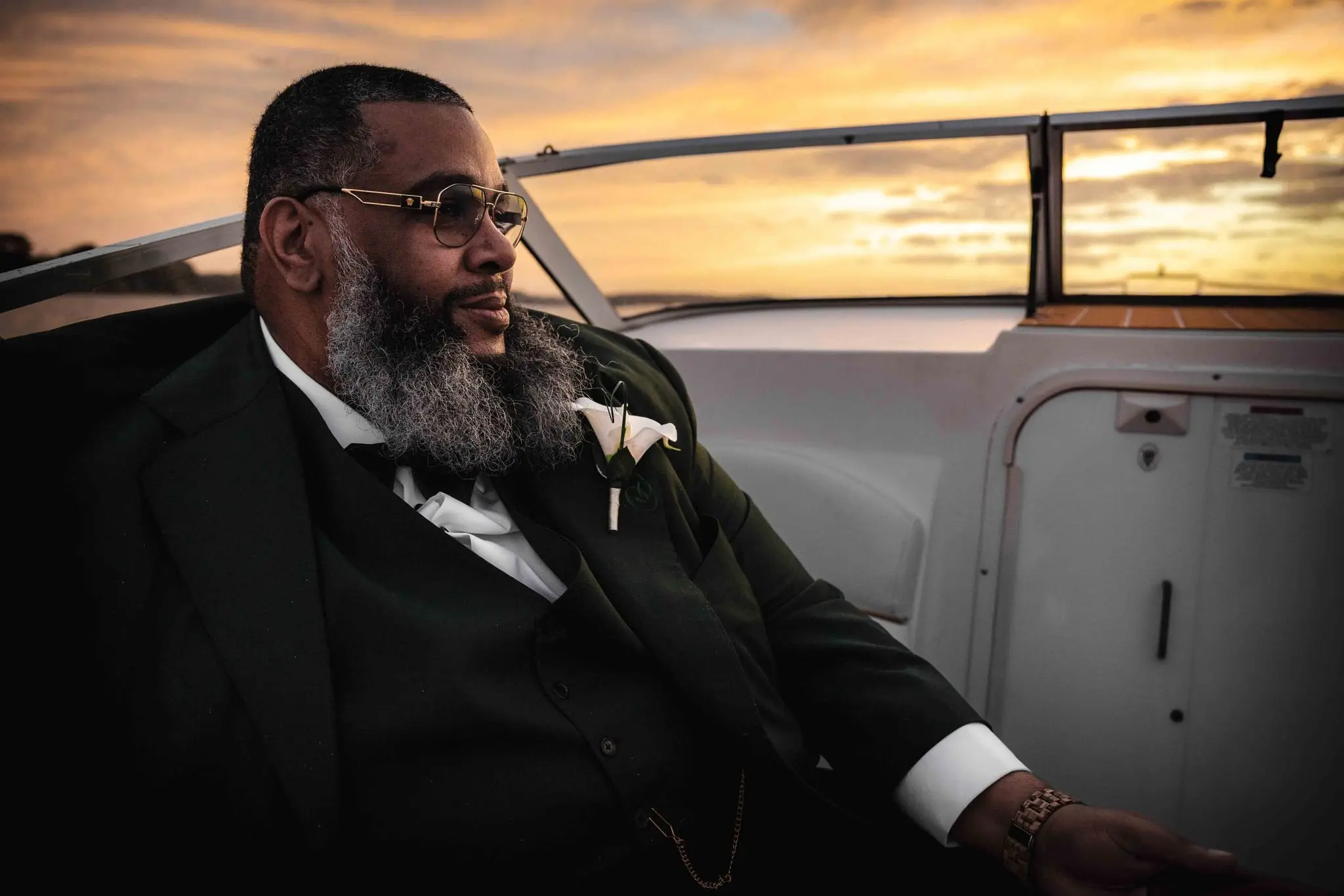 Groom in glasses and a green three-piece suit gazing across the water from the boat