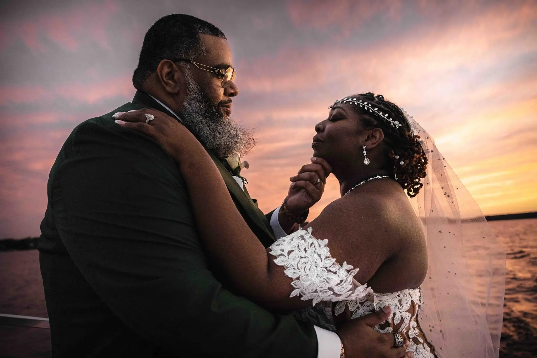 Crystal and Na'im embracing at sunset under a pink and orange sky over the water