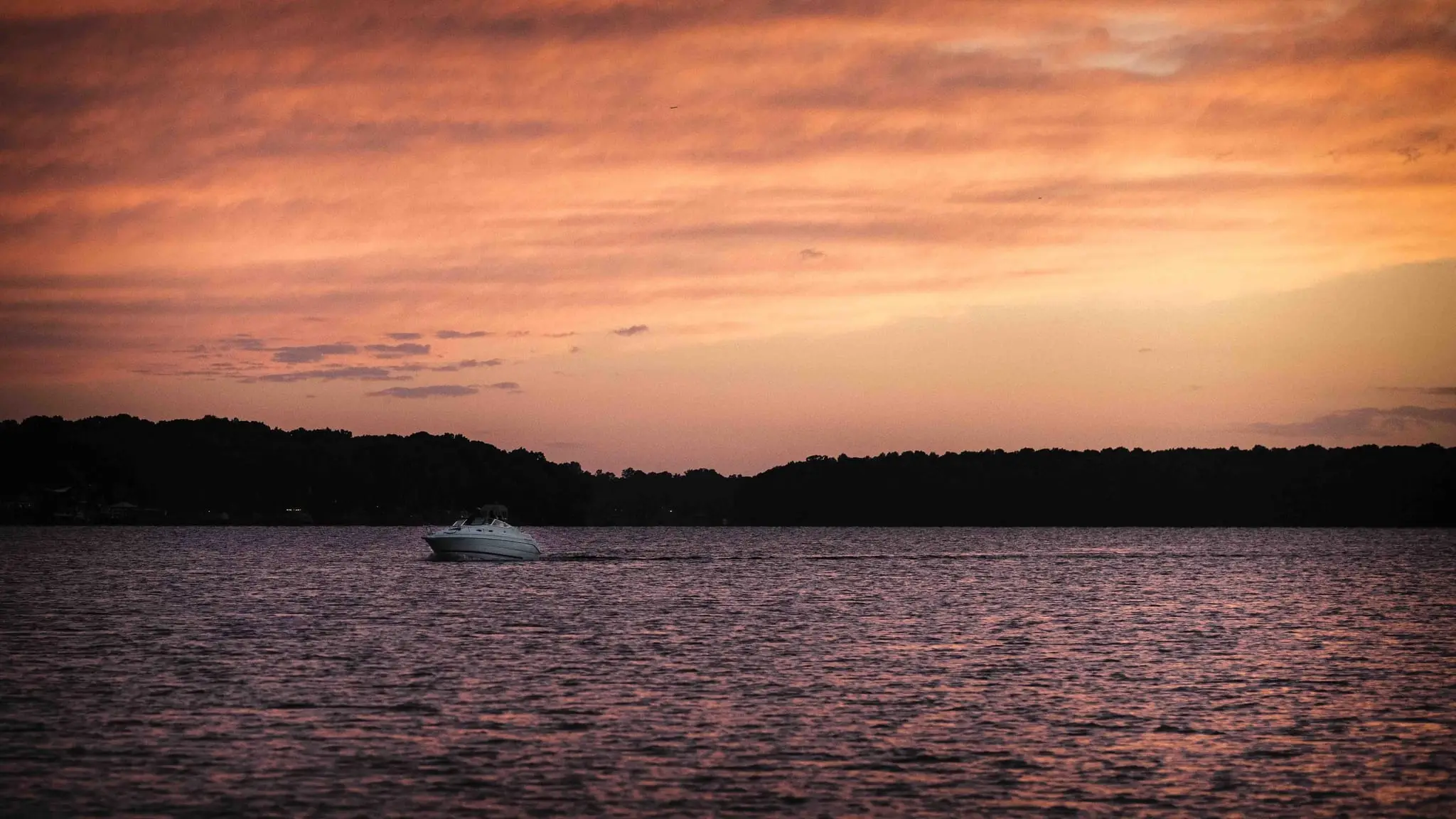 Pink and orange sunset sky over the lake with a distant boat leaving a wake