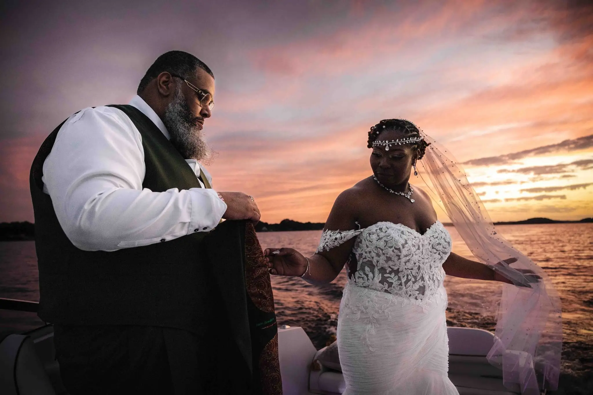 Bride's veil blowing as the groom lifts his green jacket around her on the boat