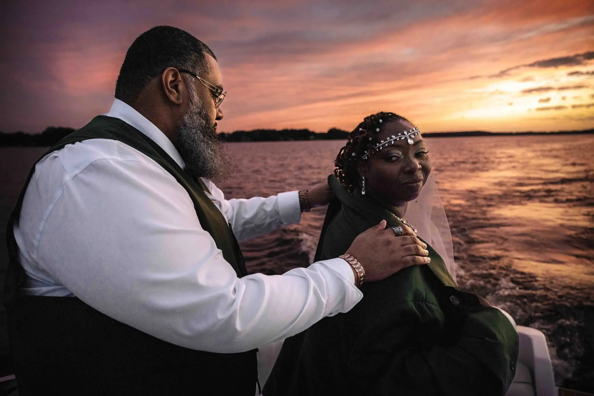 Groom resting his hands on the bride's shoulders over the jacket as she glances back at him