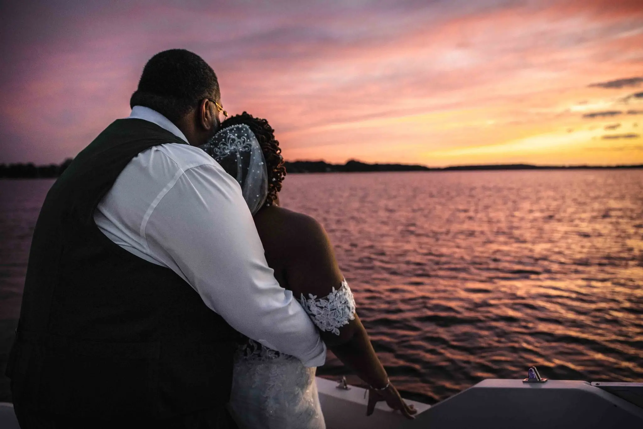 Couple embracing at the boat's edge with the lake and sunset ahead