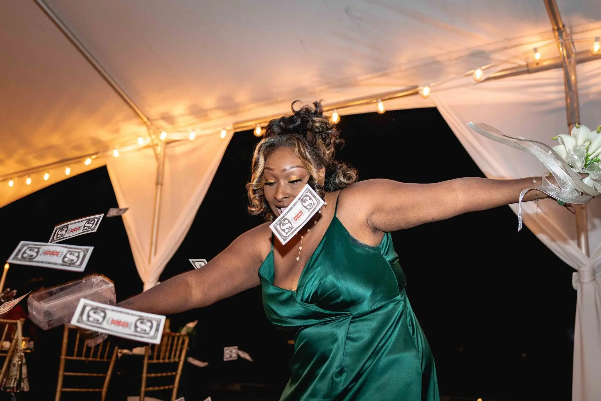 Bridesmaid in emerald satin dancing under the reception tent with dollar bills falling around her