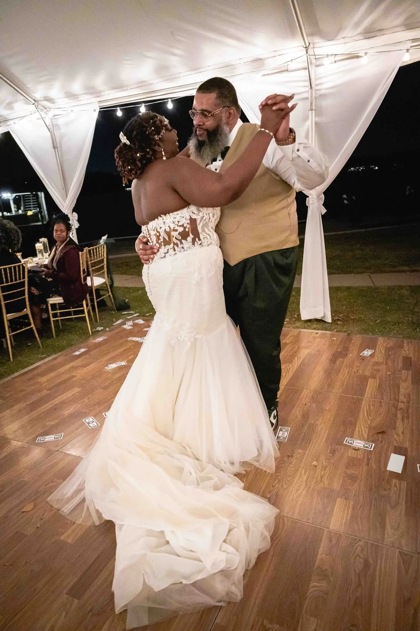 Couple's first dance on a wood floor under the string-lit tent, her long train spread behind