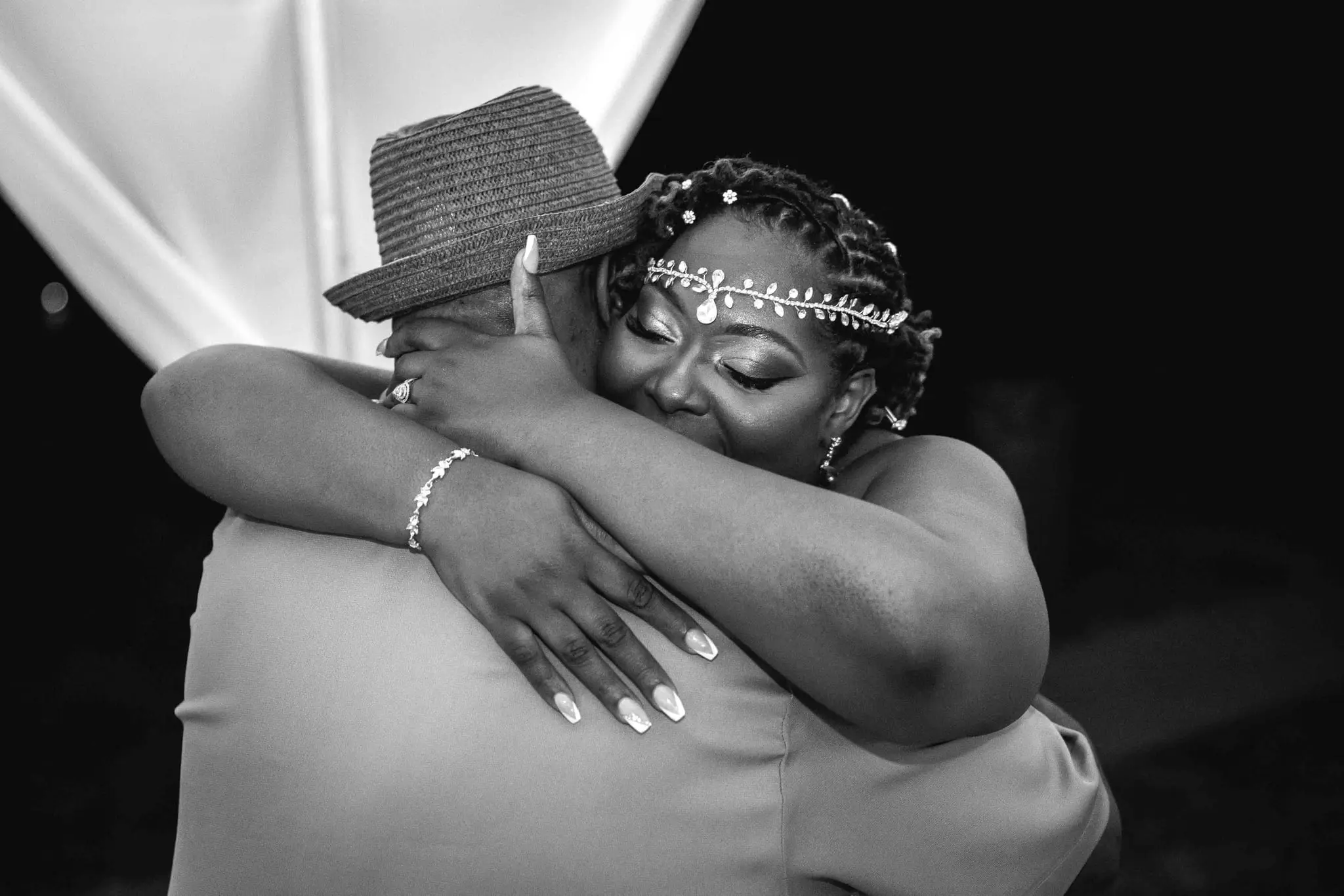 Black and white of the bride hugging a guest in a fedora, eyes closed