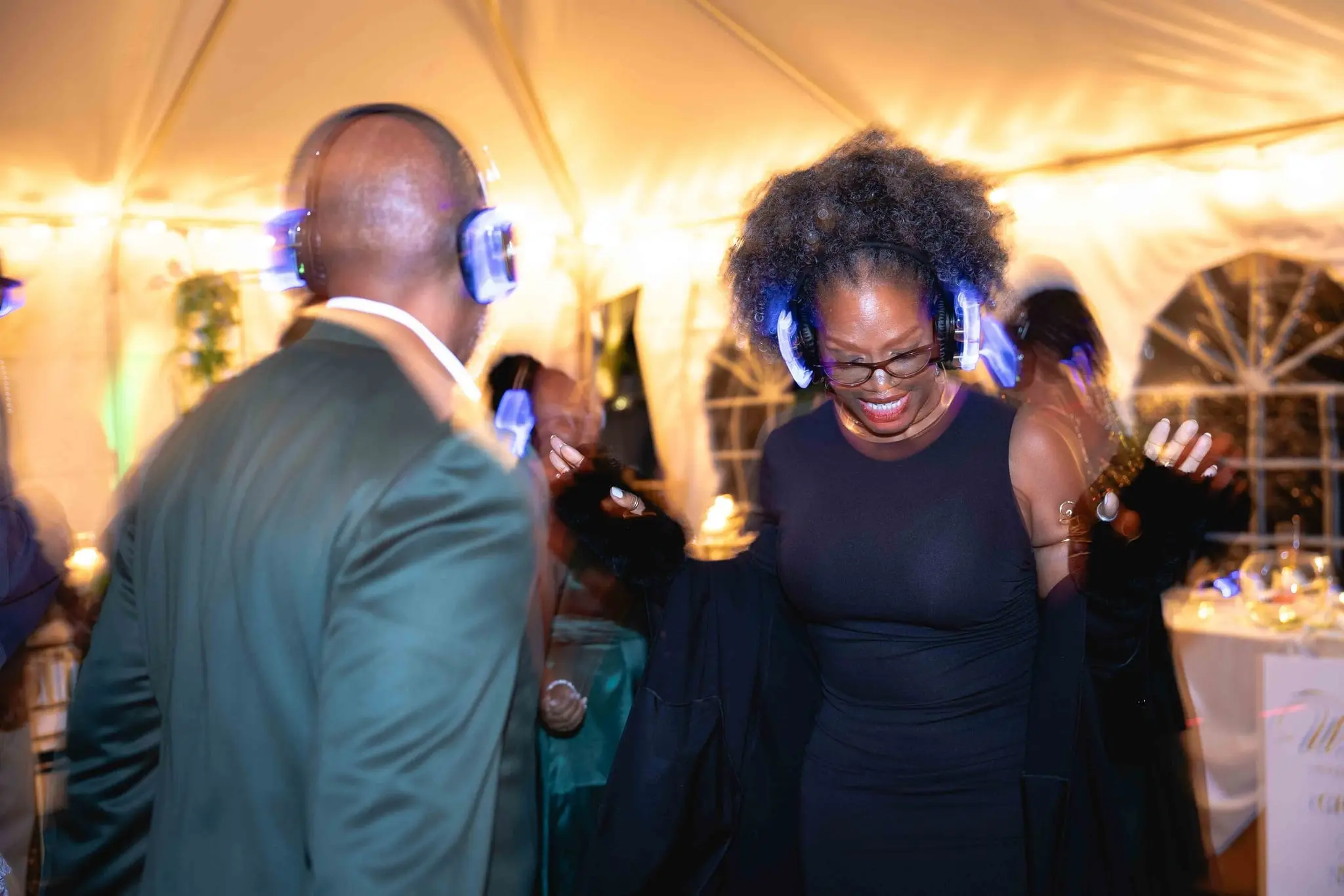 Guests dancing and laughing in glowing headphones under the string-lit tent