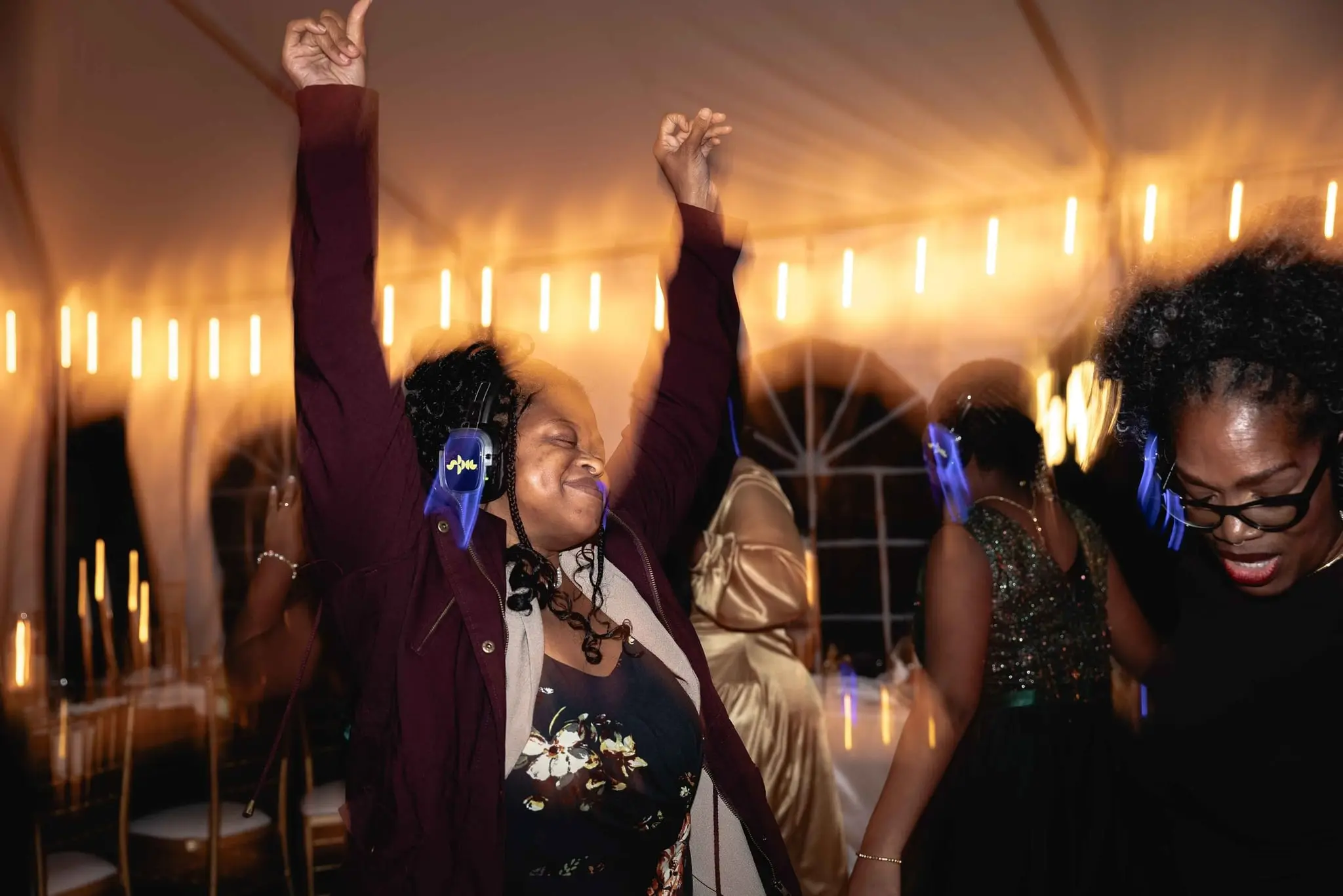 Guest in a burgundy jacket throwing her arms up on the dance floor in silent disco headphones