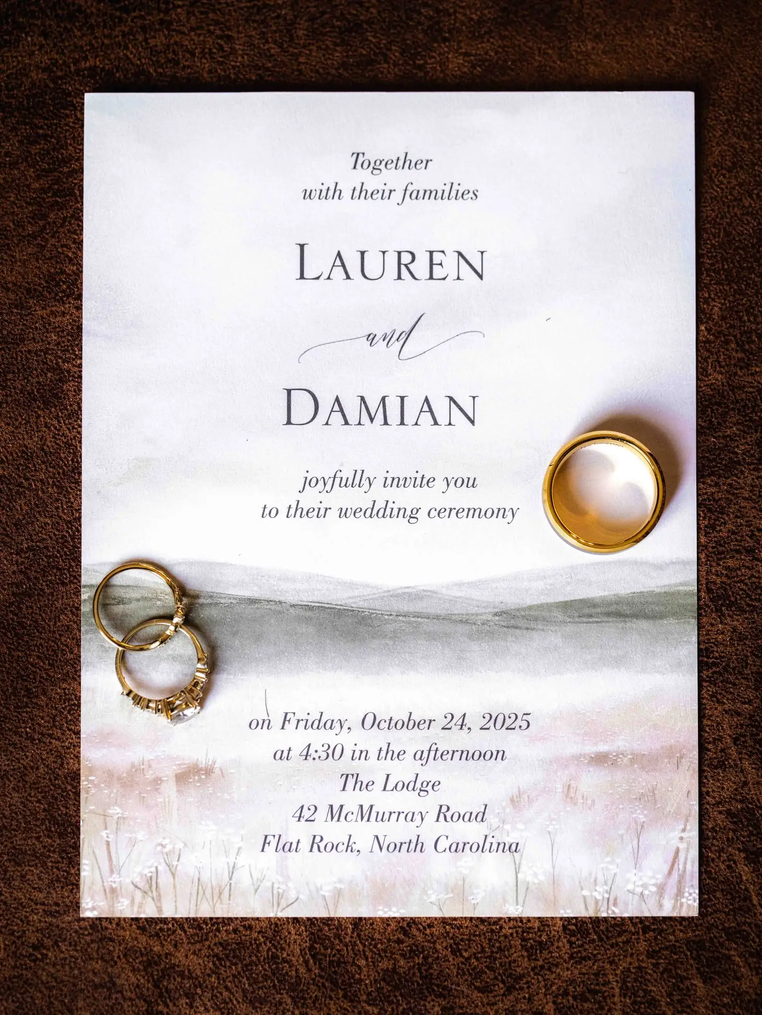 Lauren and Damian wedding at The Lodge at Flat Rock, Flat Rock NC — the wedding invitation and two rings on a brown leather surface