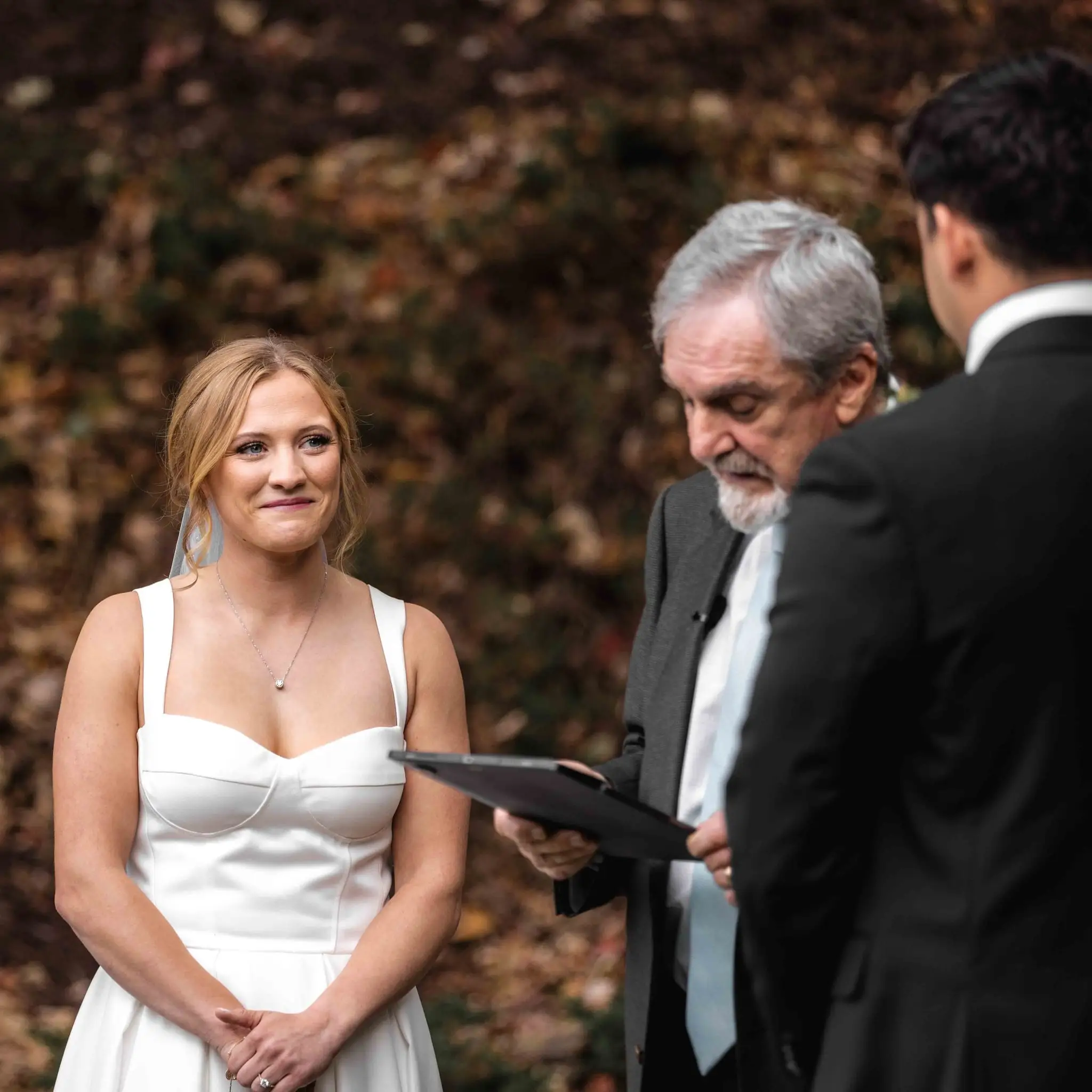 Lauren and Damian wedding at The Lodge at Flat Rock, Flat Rock NC — the bride smiling at the officiant during the vows