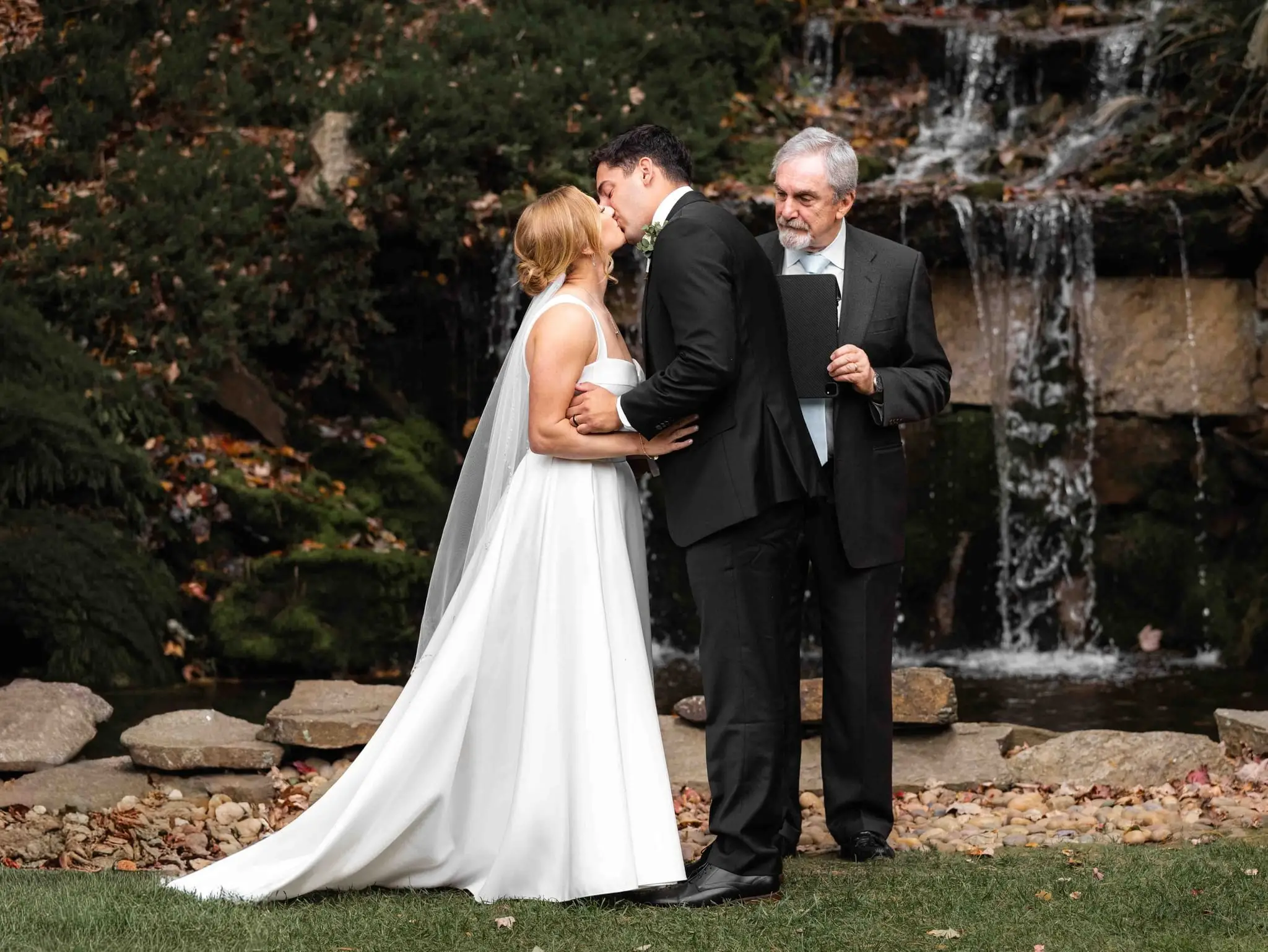 Couple’s first kiss beside a waterfall during their ceremony at The Lodge at Flat Rock