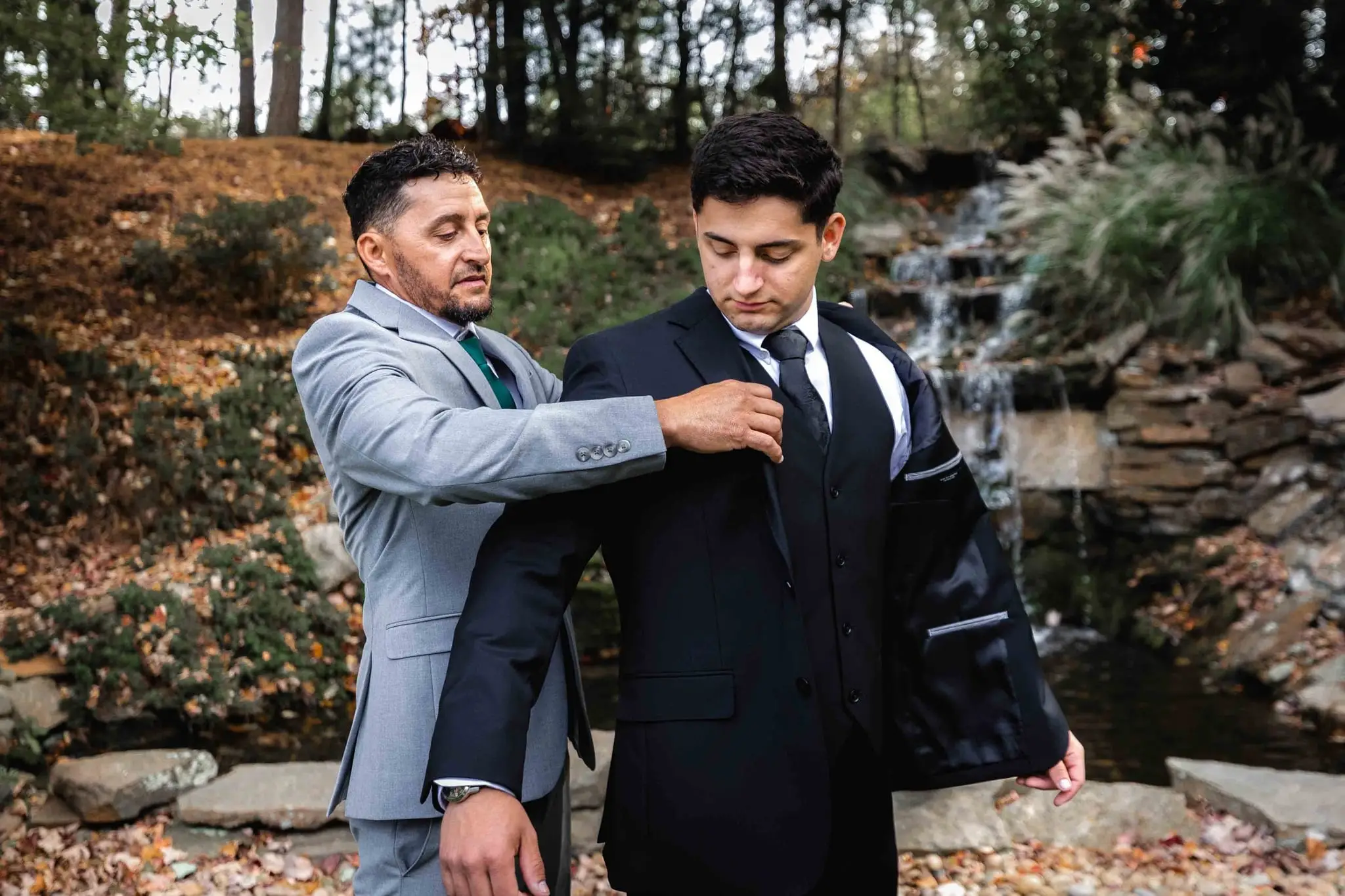 Lauren and Damian wedding at The Lodge at Flat Rock, Flat Rock NC — a groomsman straightening the groom's tie beside a rock waterfall