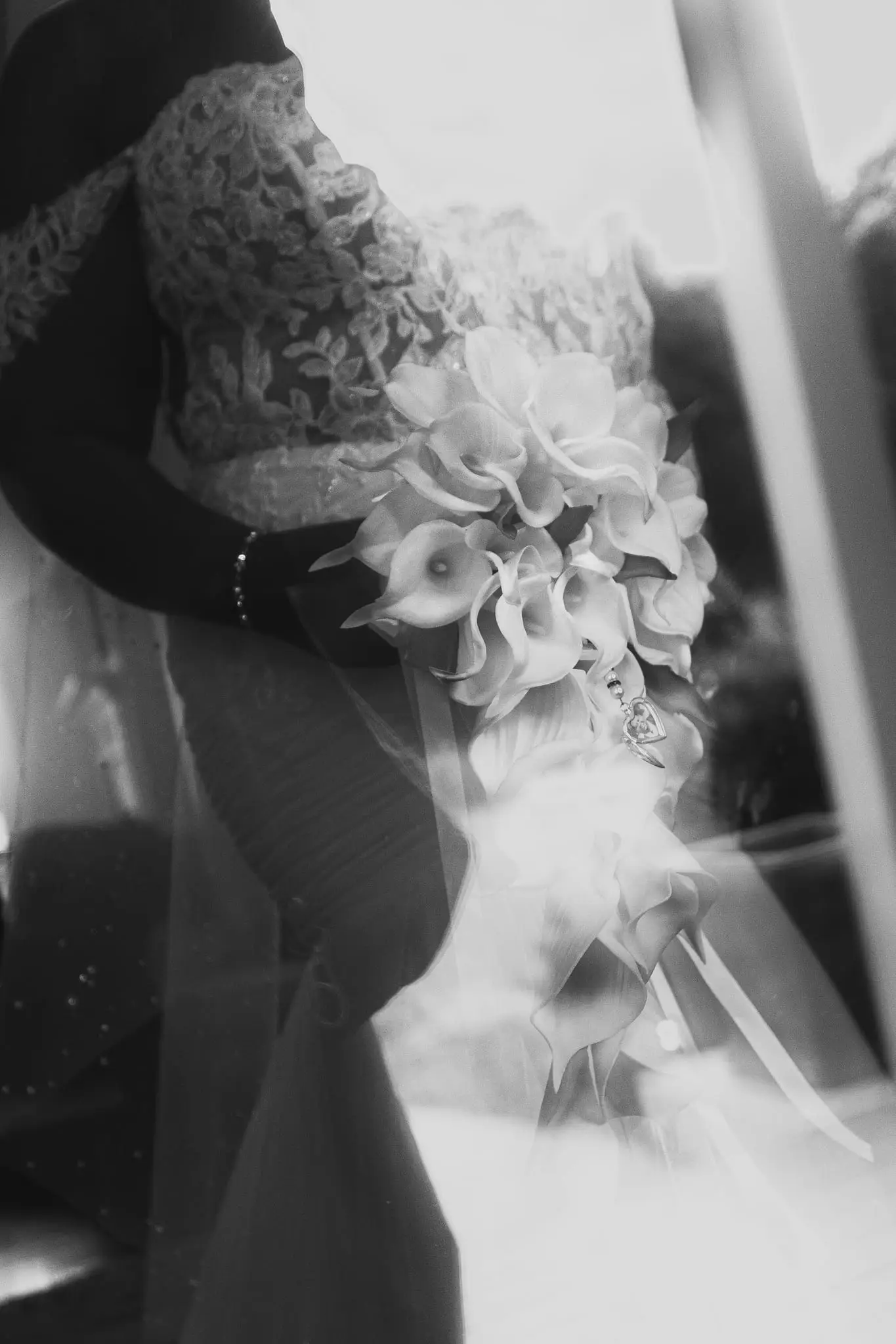 Black and white detail of a bride's calla lily bouquet, wedding ring and beaded bracelet