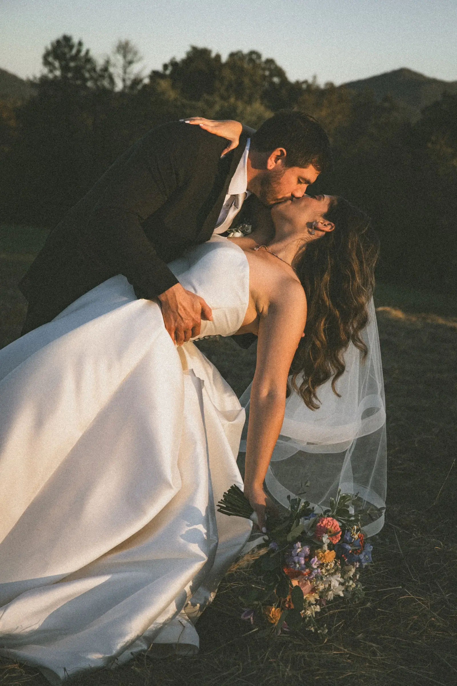 Groom dipping the bride for a kiss in a field at golden hour