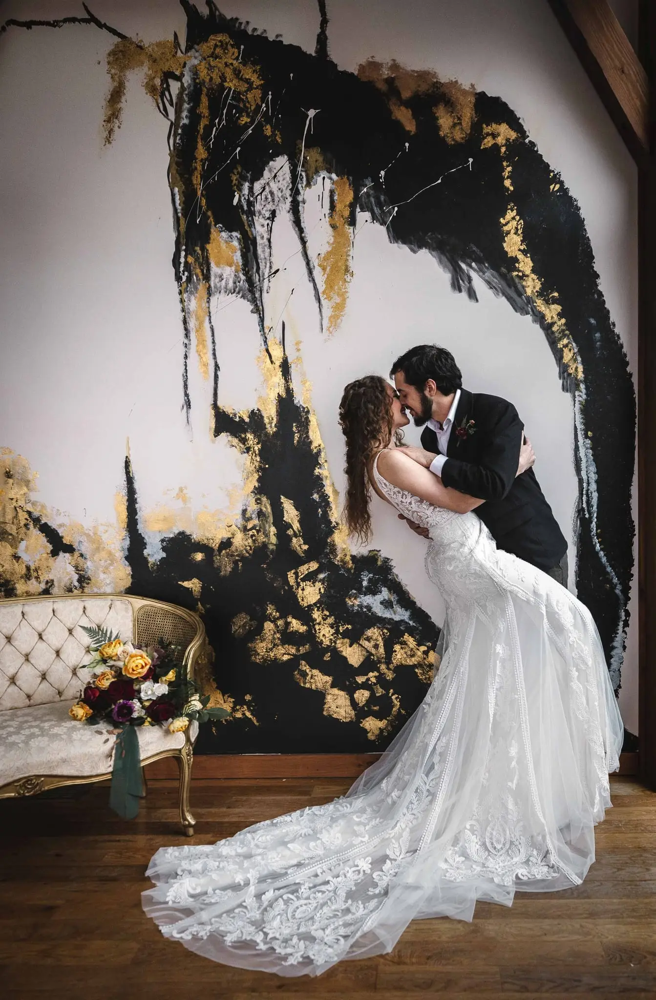 Joe and Julia at Haiku I Do, Asheville NC — a couple kissing in front of a painted gold-and-black wall, the bride's long train spread on the floor