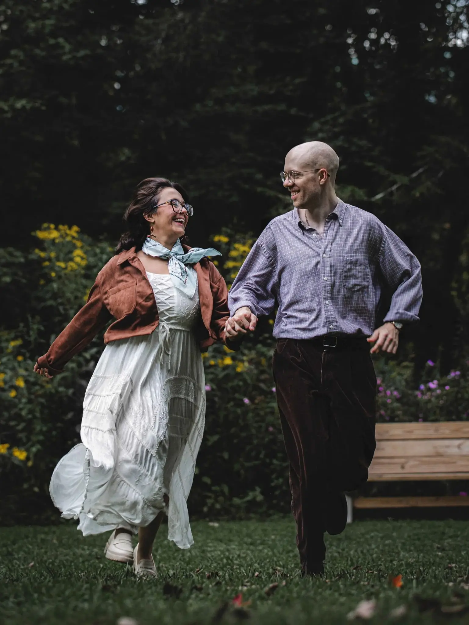 Couple running hand in hand and laughing across a garden lawn