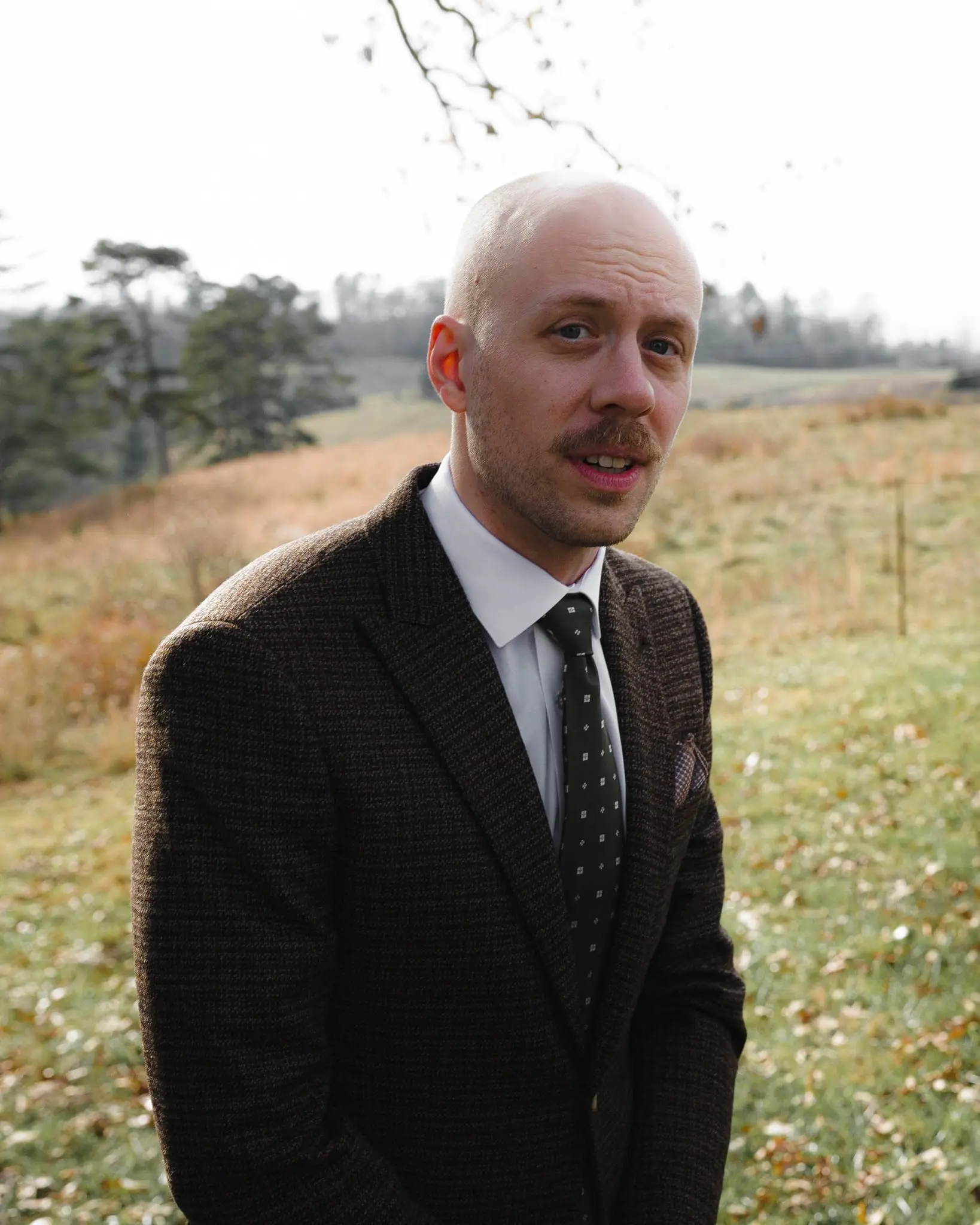 Portrait of the groom in a brown tweed jacket and green tie in front of a rolling Weaverville pasture