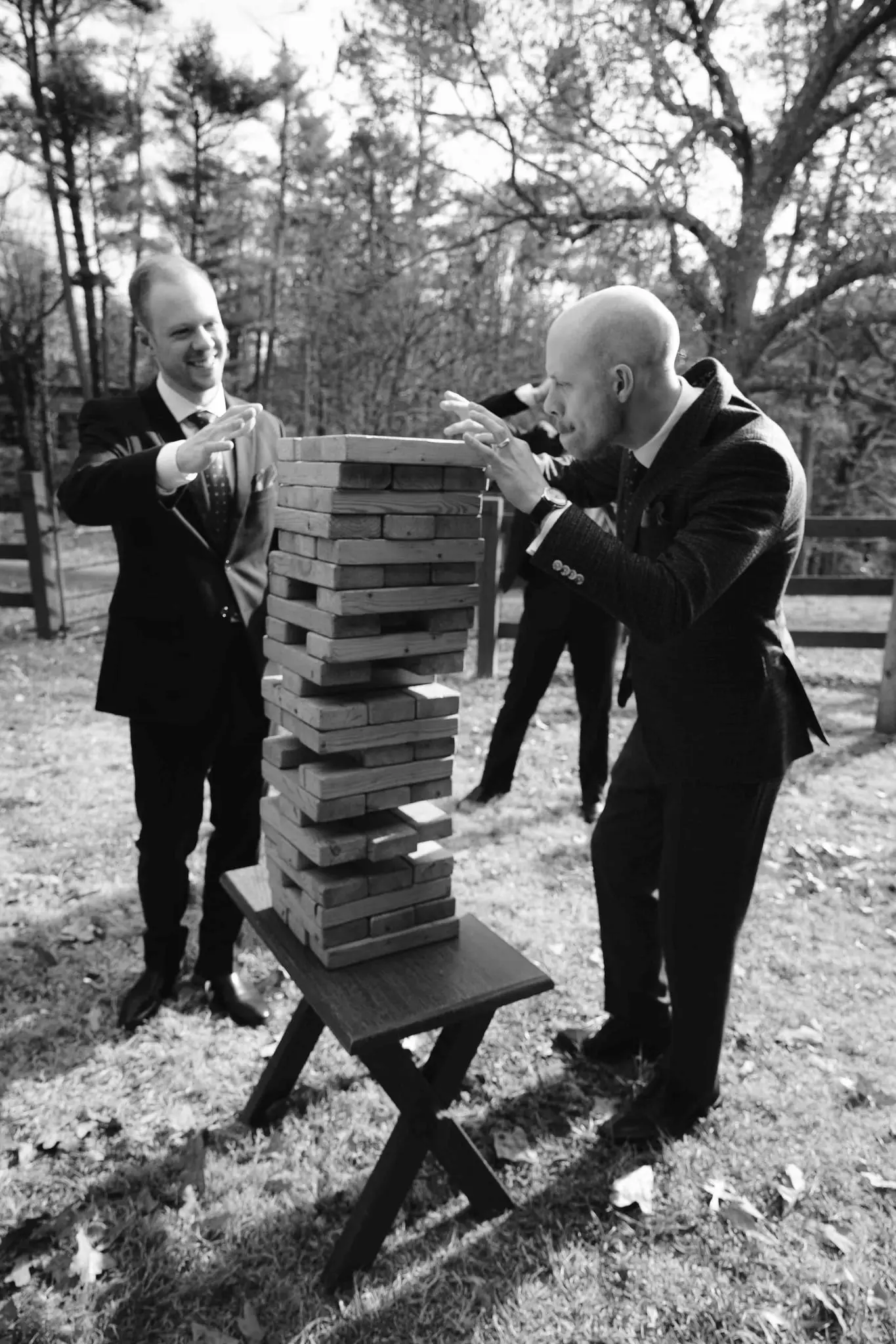 Black and white groomsmen play a giant Jenga tower on the lawn