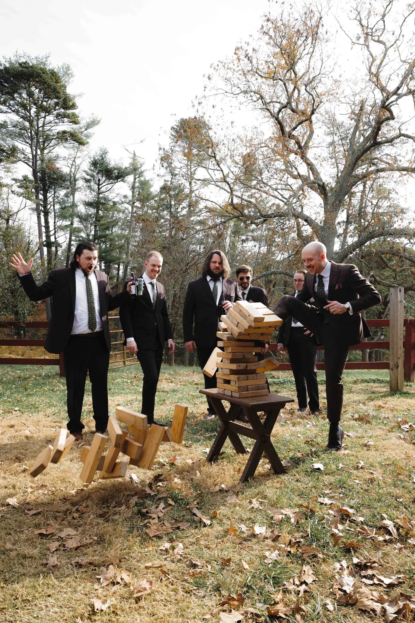 Groomsmen jump back as the giant Jenga tower collapses on the grass